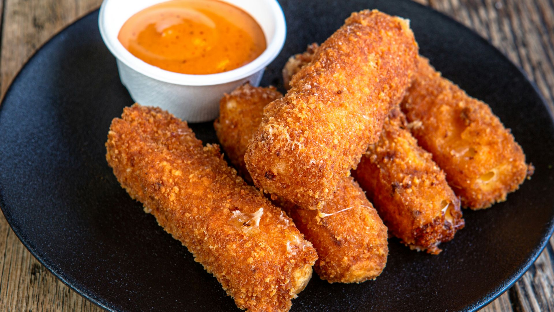 A black plate topped with fried food next to a cup of dipping sauce