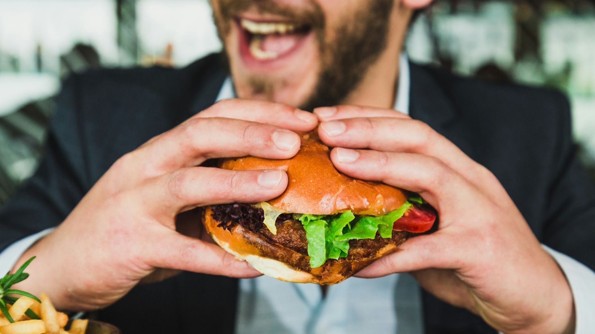 person holding burger bun with vegetables and meat