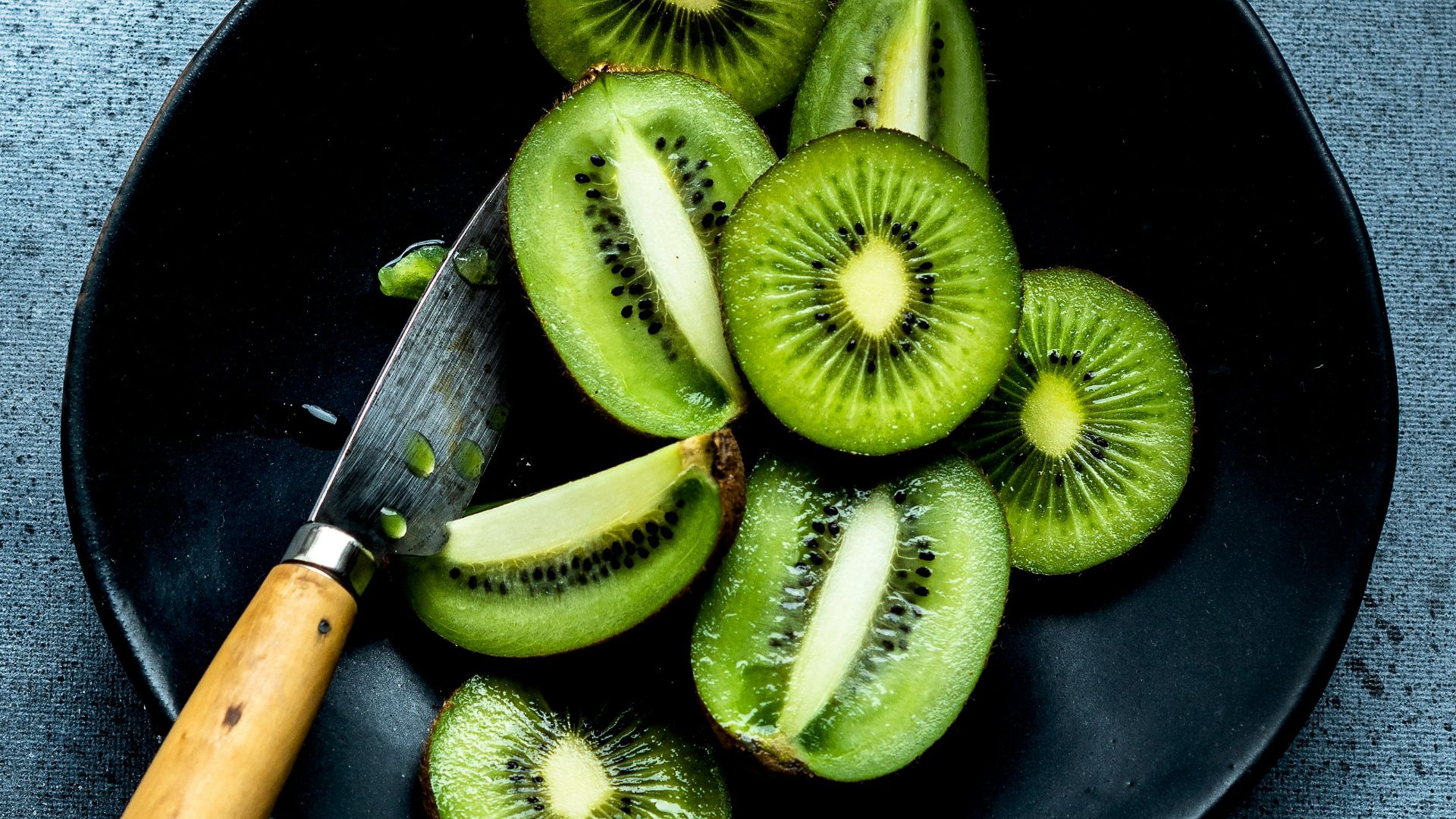 a black plate topped with sliced kiwis and a knife