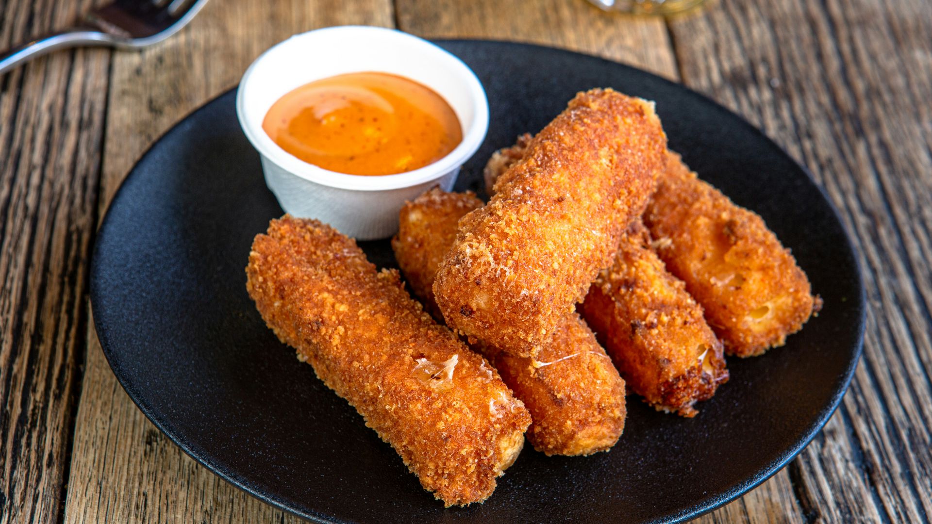 A black plate topped with fried food next to a cup of dipping sauce