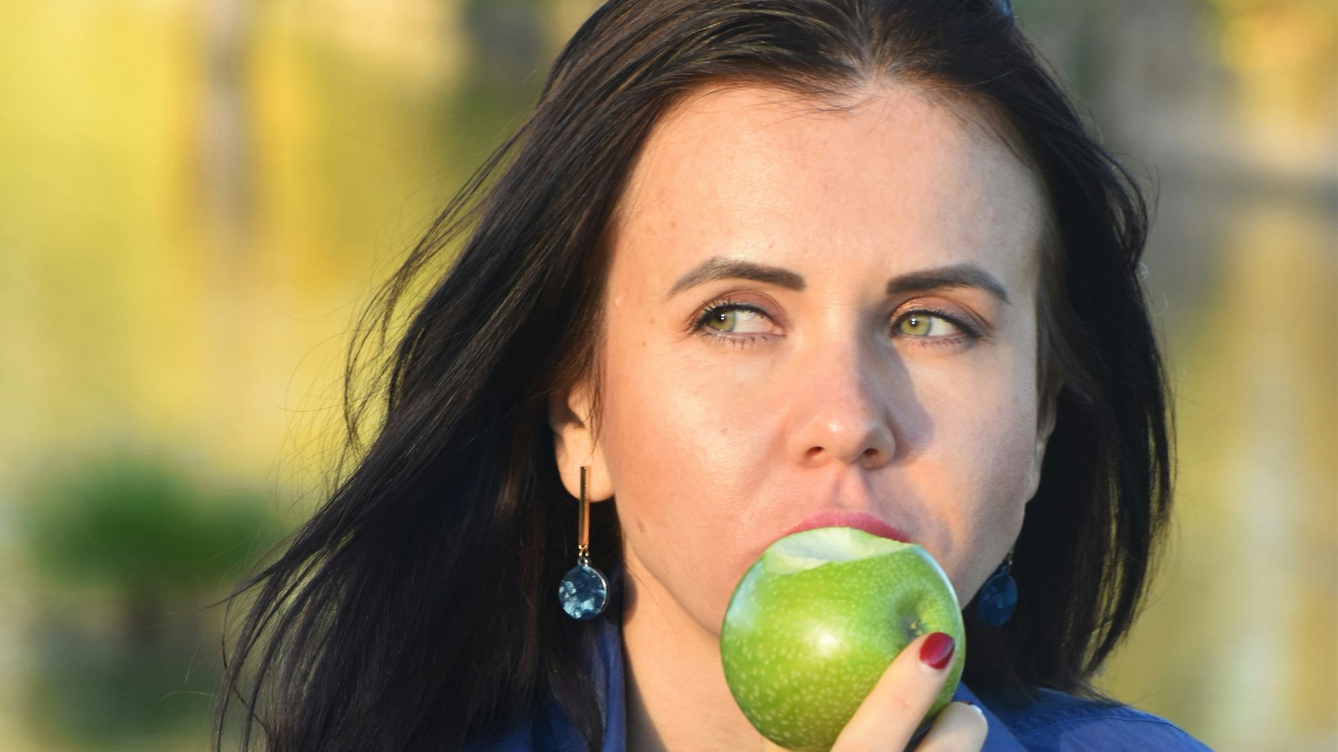 a woman in a blue shirt eating an apple