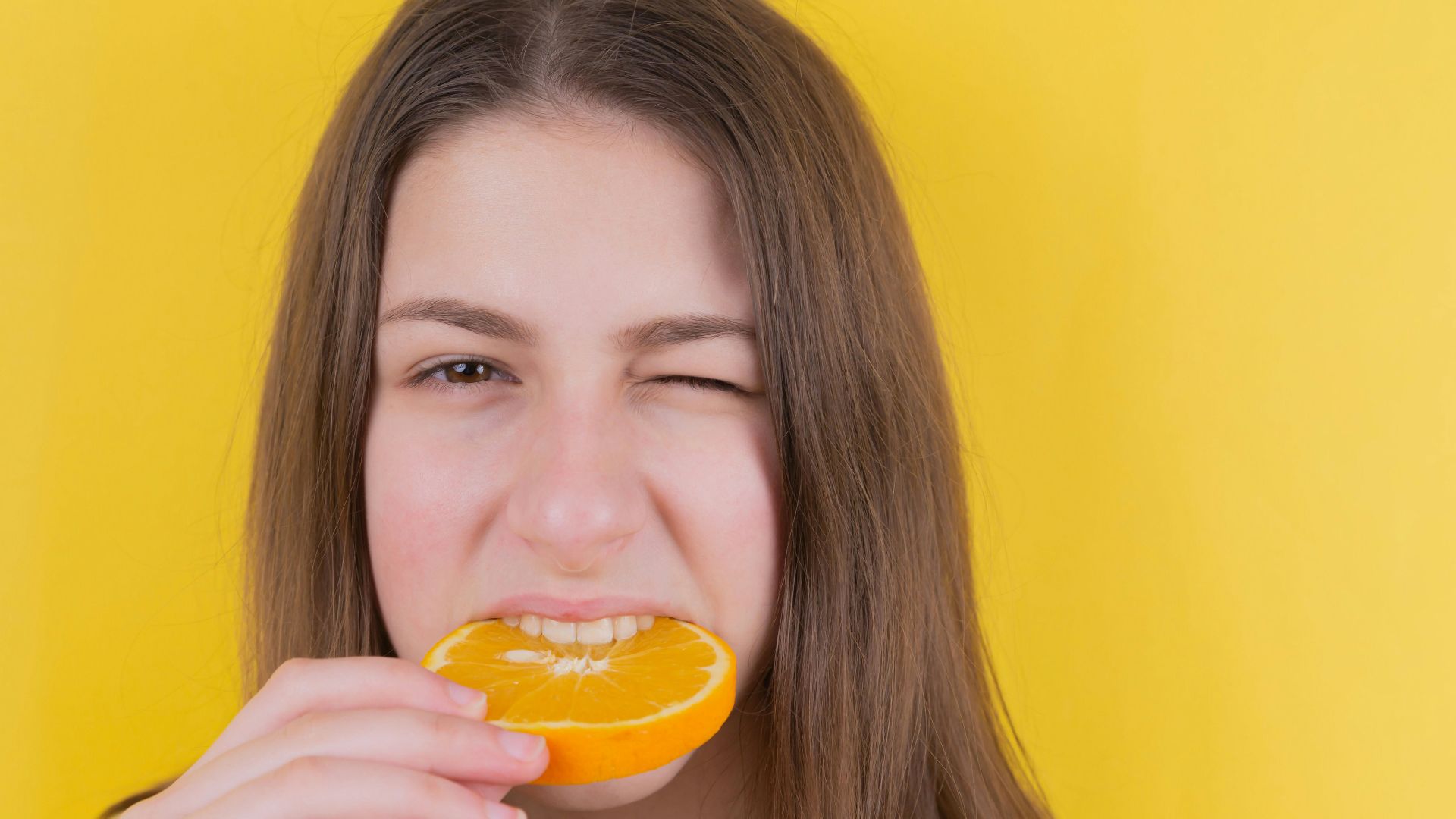girl holding orange fruit in front of yellow wall