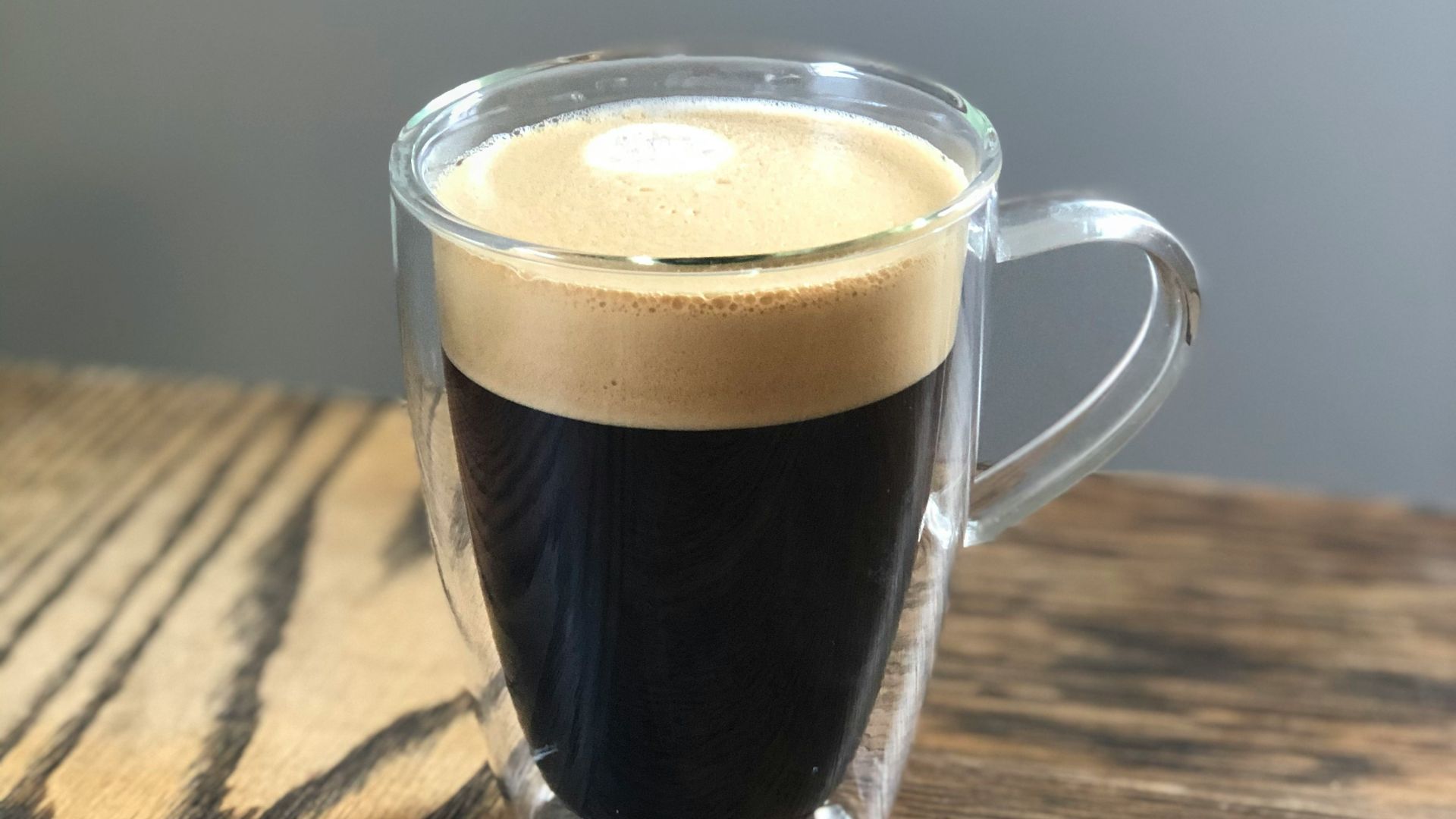 clear glass mug with brown liquid on brown wooden table