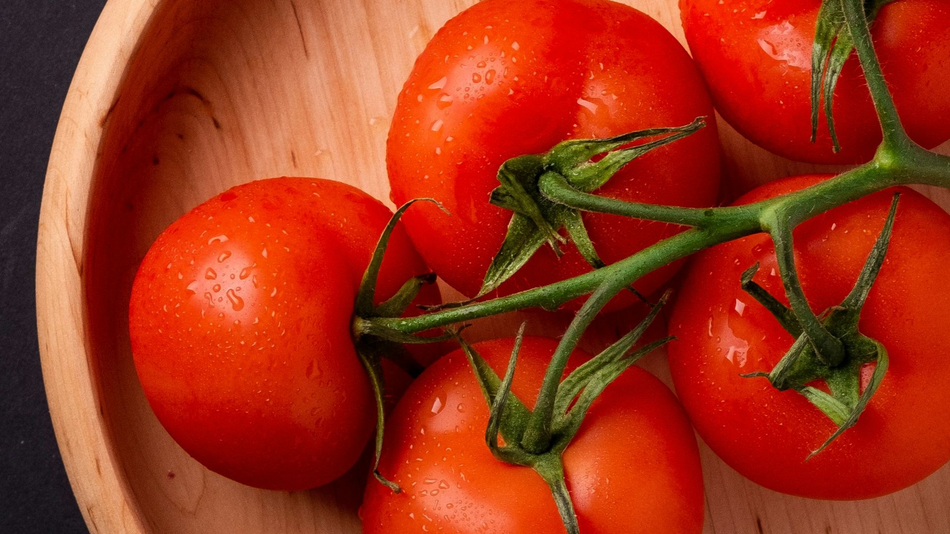 five tomatoes in round brown wooden platet