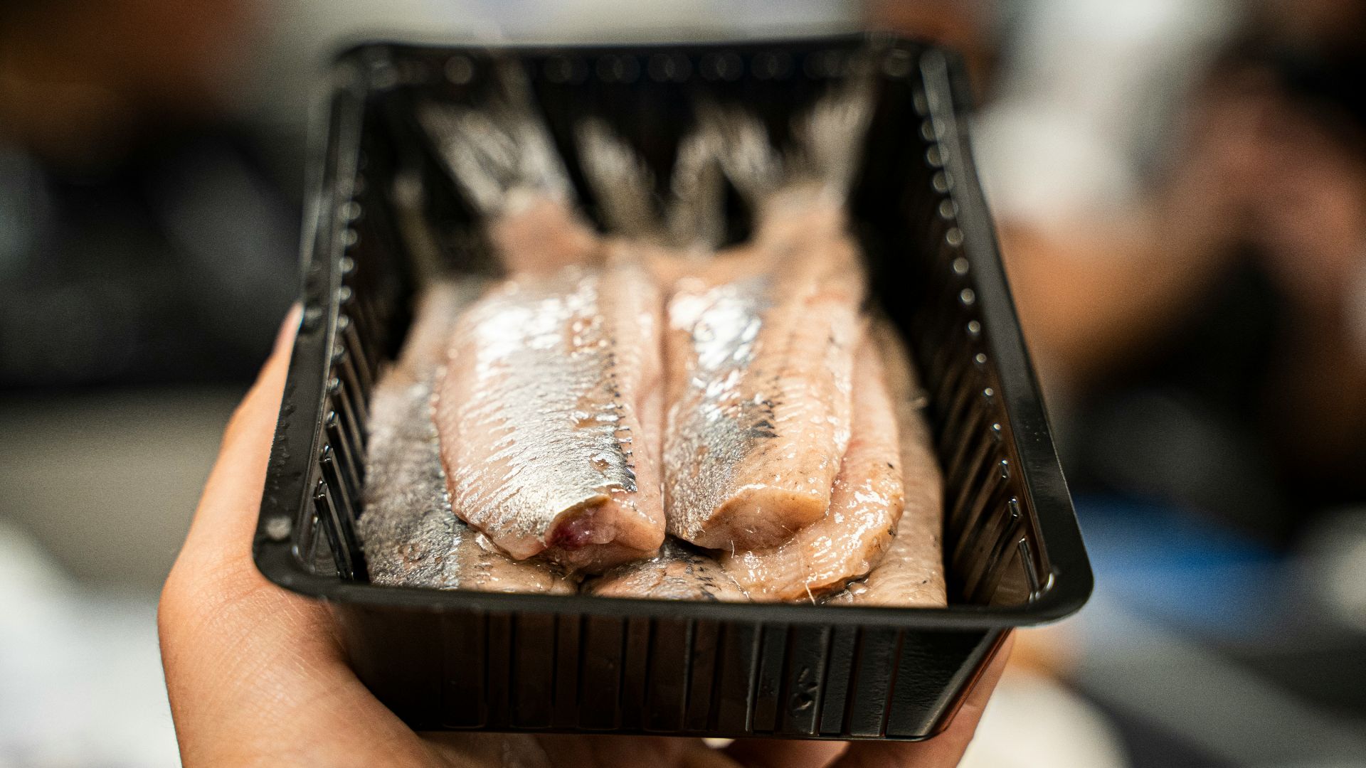 person holding black plastic tray with meat