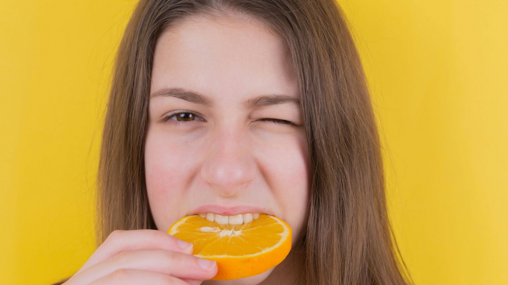 girl holding orange fruit in front of yellow wall