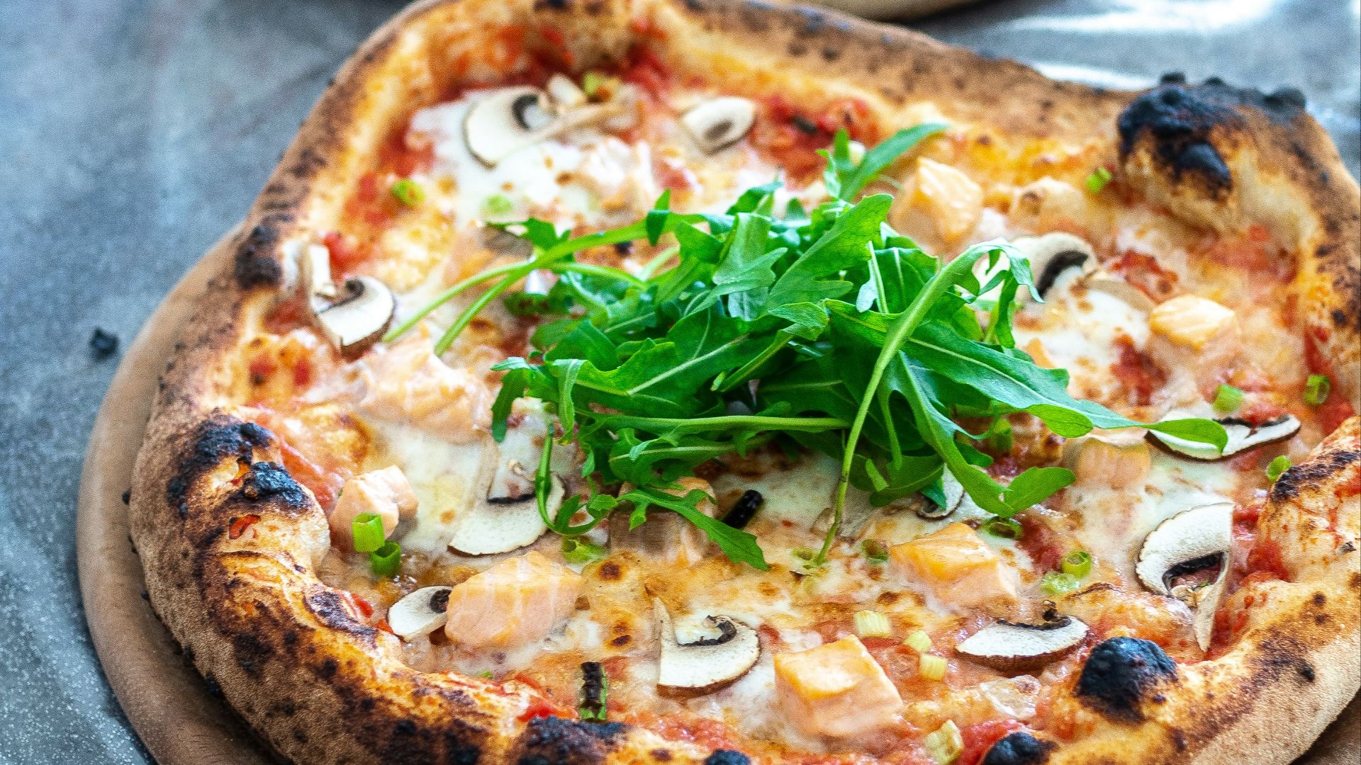 pizza with green leaves on brown wooden table