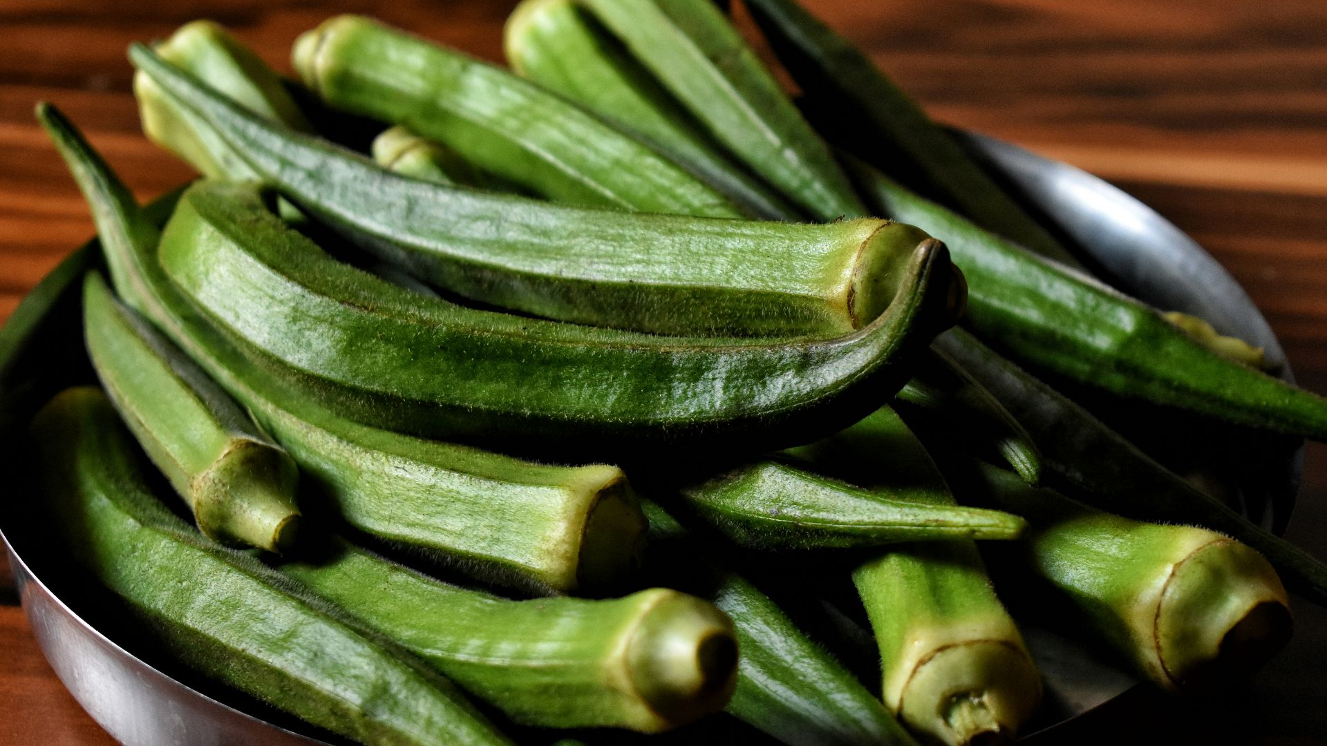 a metal bowl filled with green beans on top of a wooden table