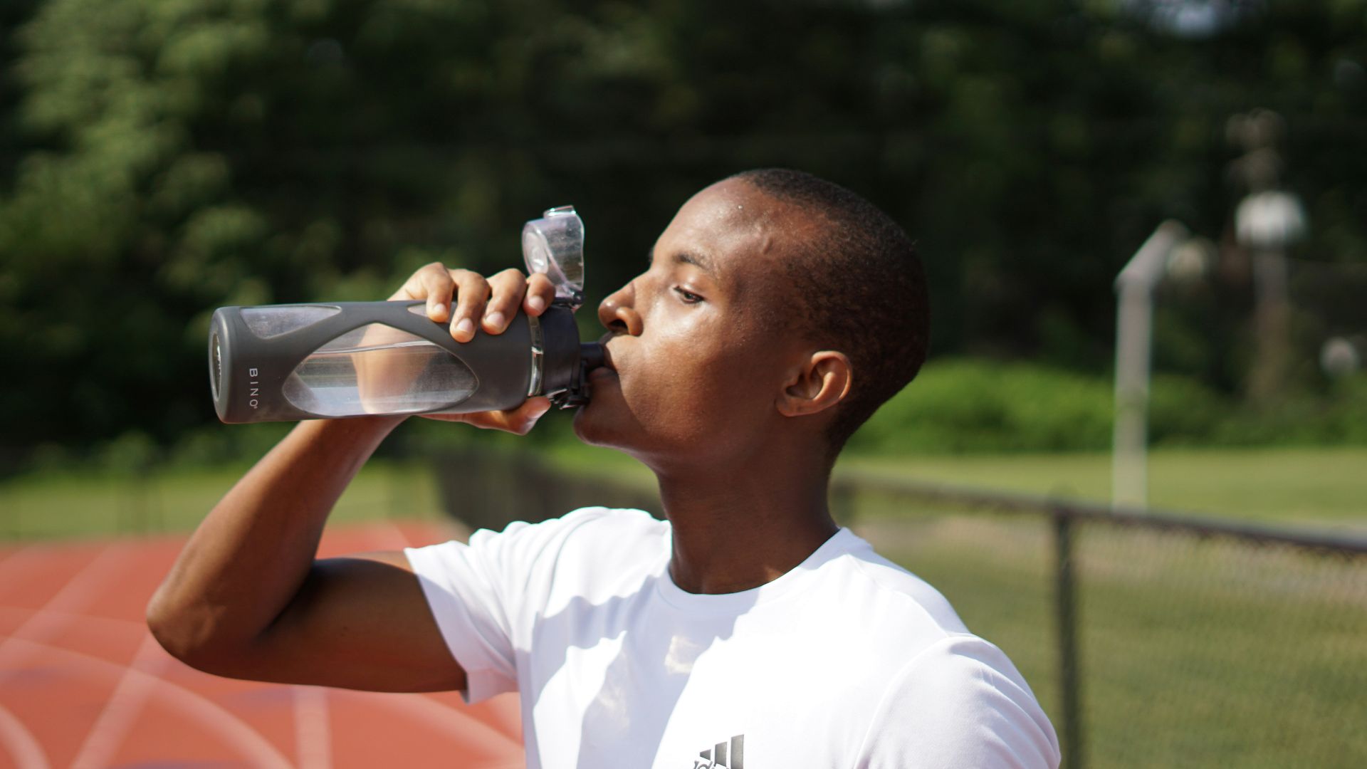 man in white crew neck t-shirt drinking from black sports bottle