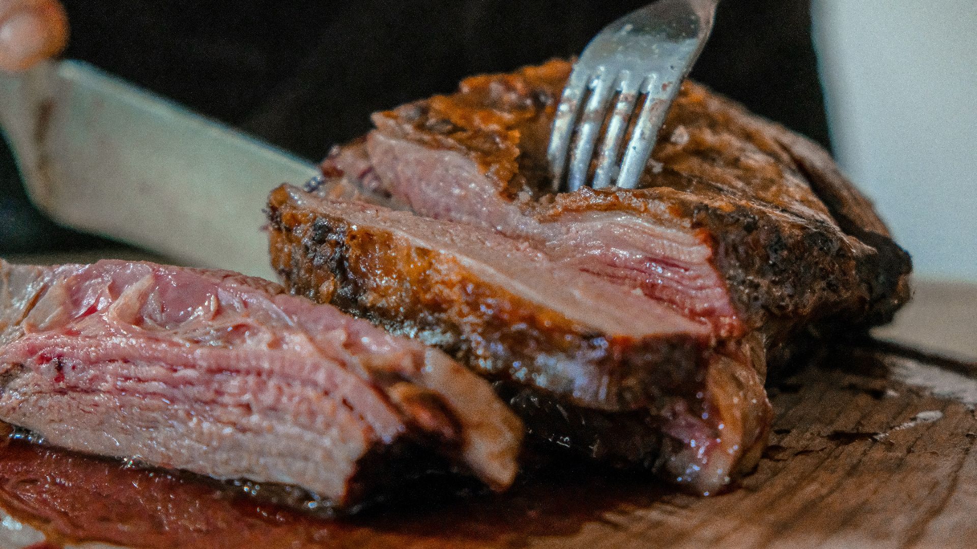 person slicing a meat on brown wooden board