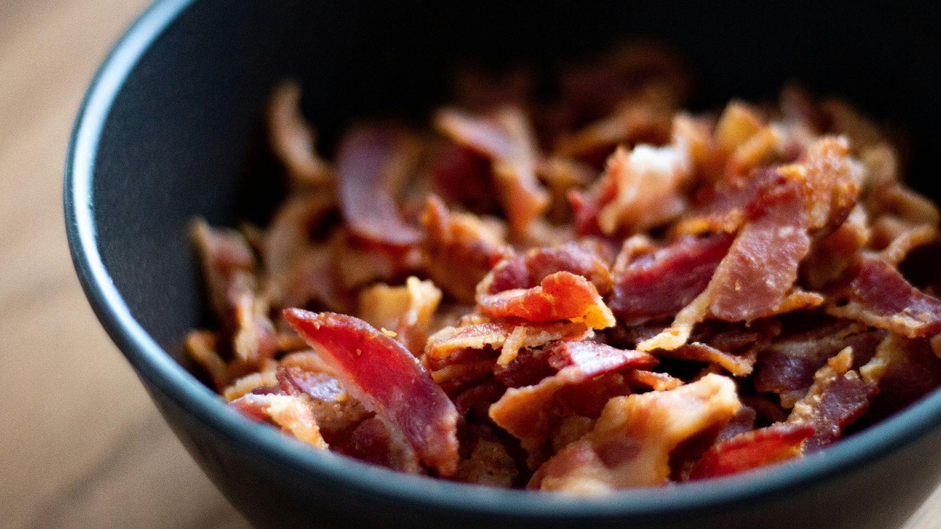Crispy bacon pieces fill a black bowl.