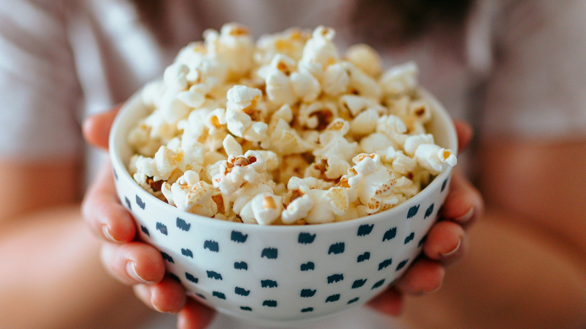 person holding white ceramic bowl with popcorn