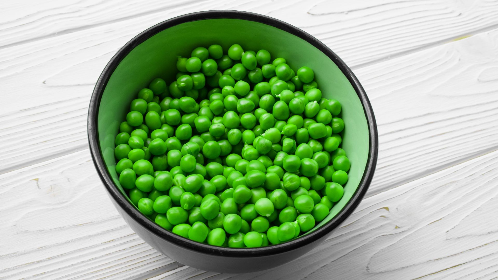 a green bowl filled with peas on top of a white table