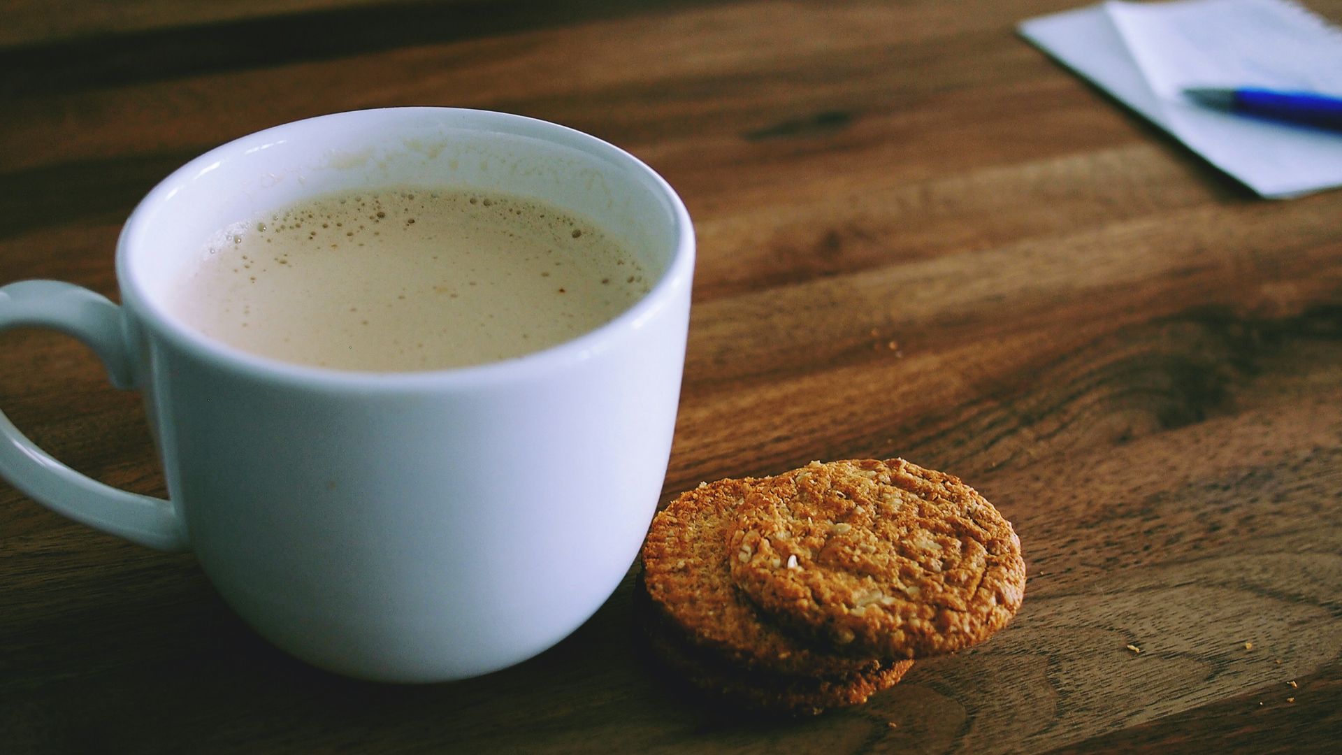 shallow focus photography of white ceramic mug beside two baked cookies on brown wooden board