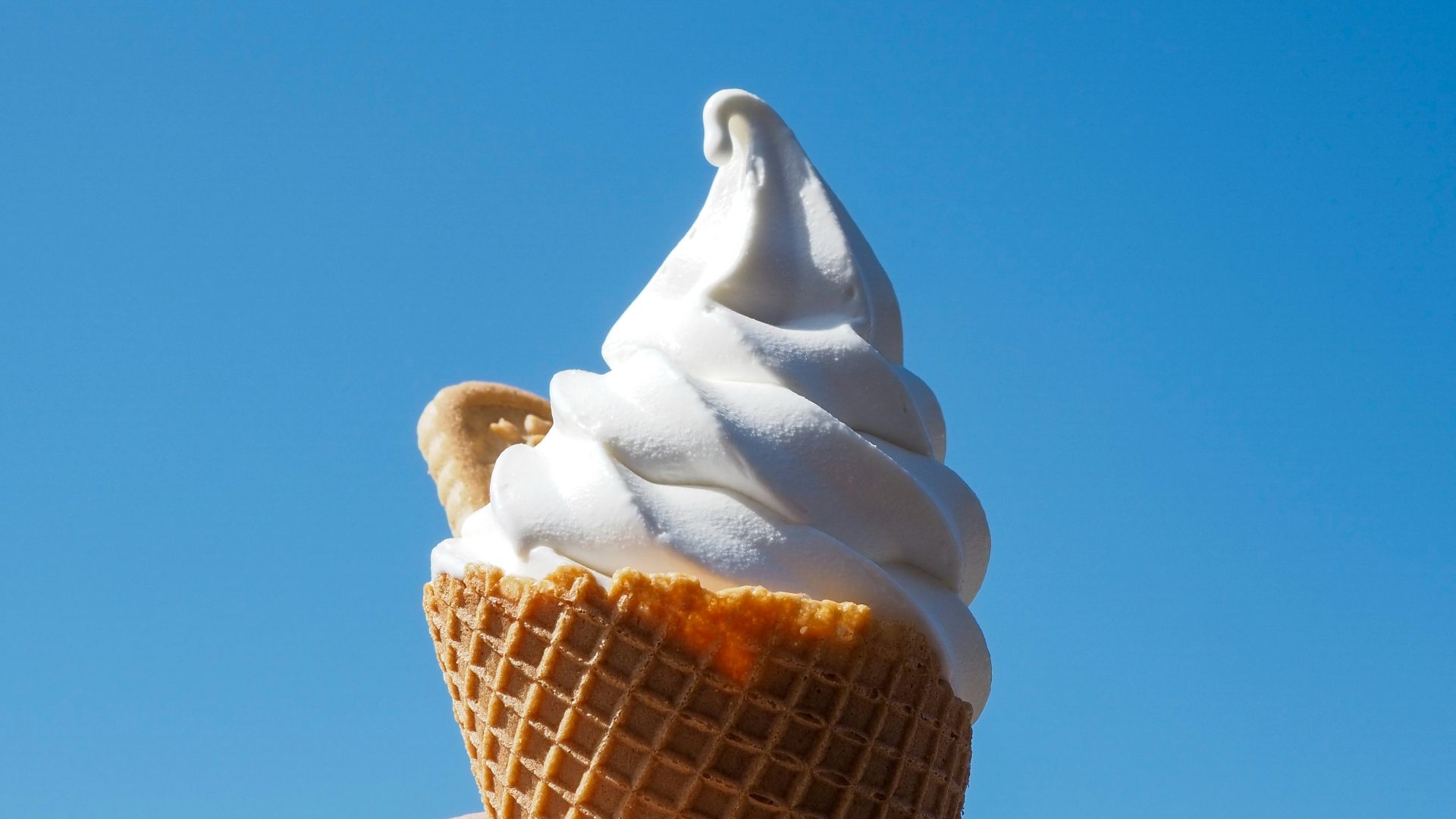 a hand holding an ice cream cone in front of a blue sky