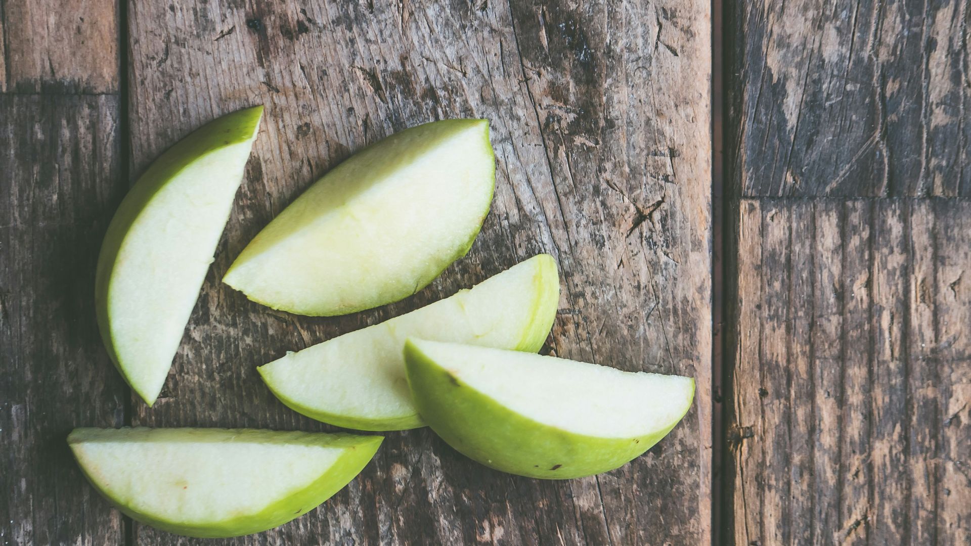 five green apple slices on brown wooden panel