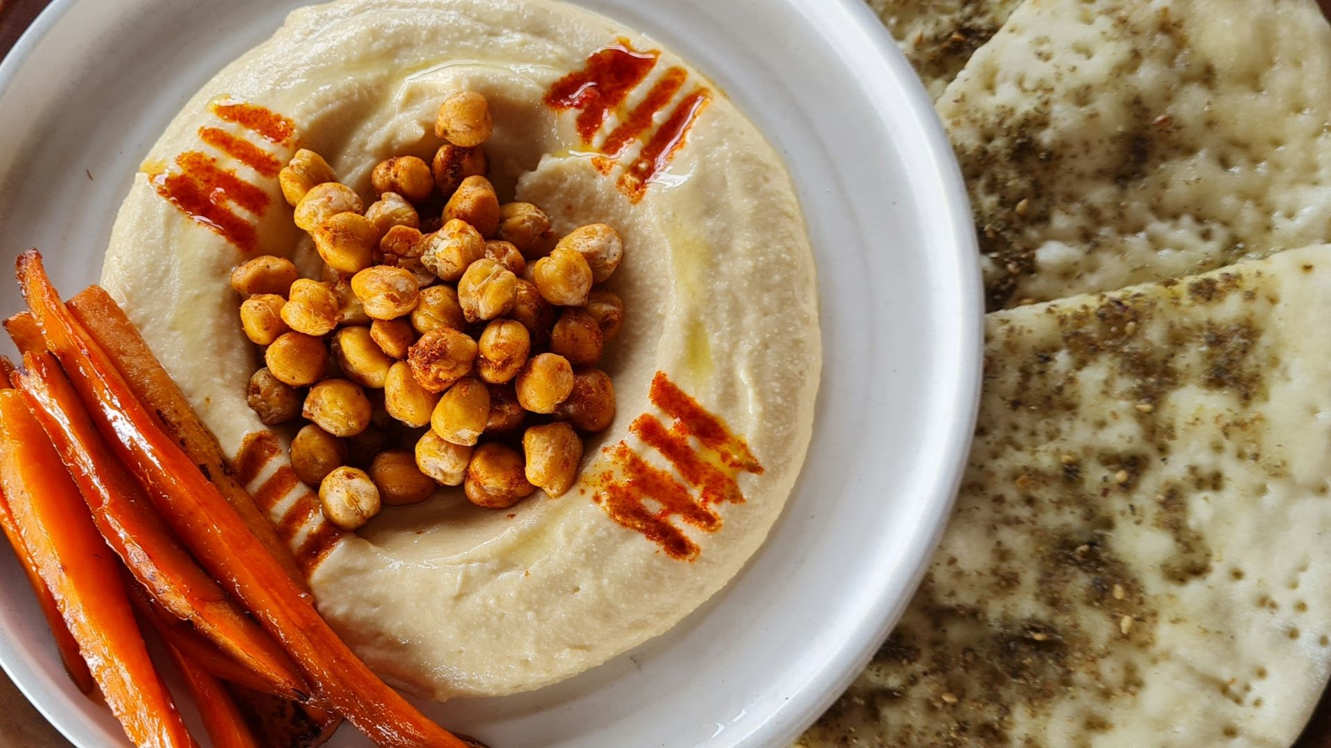 a plate of hummus, carrots, and pita bread