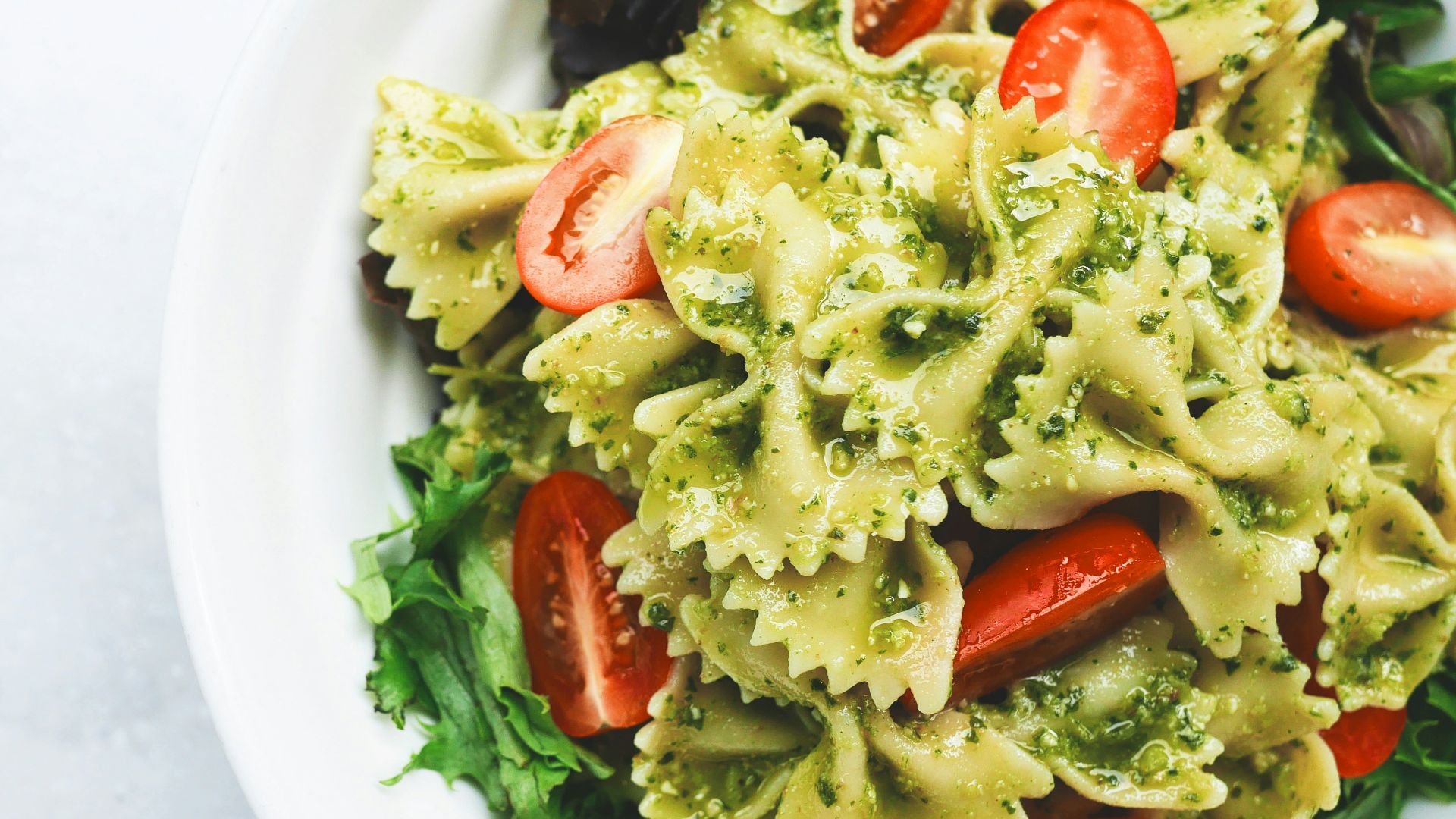 Pesto pasta with sliced tomatoes served on white ceramic plate