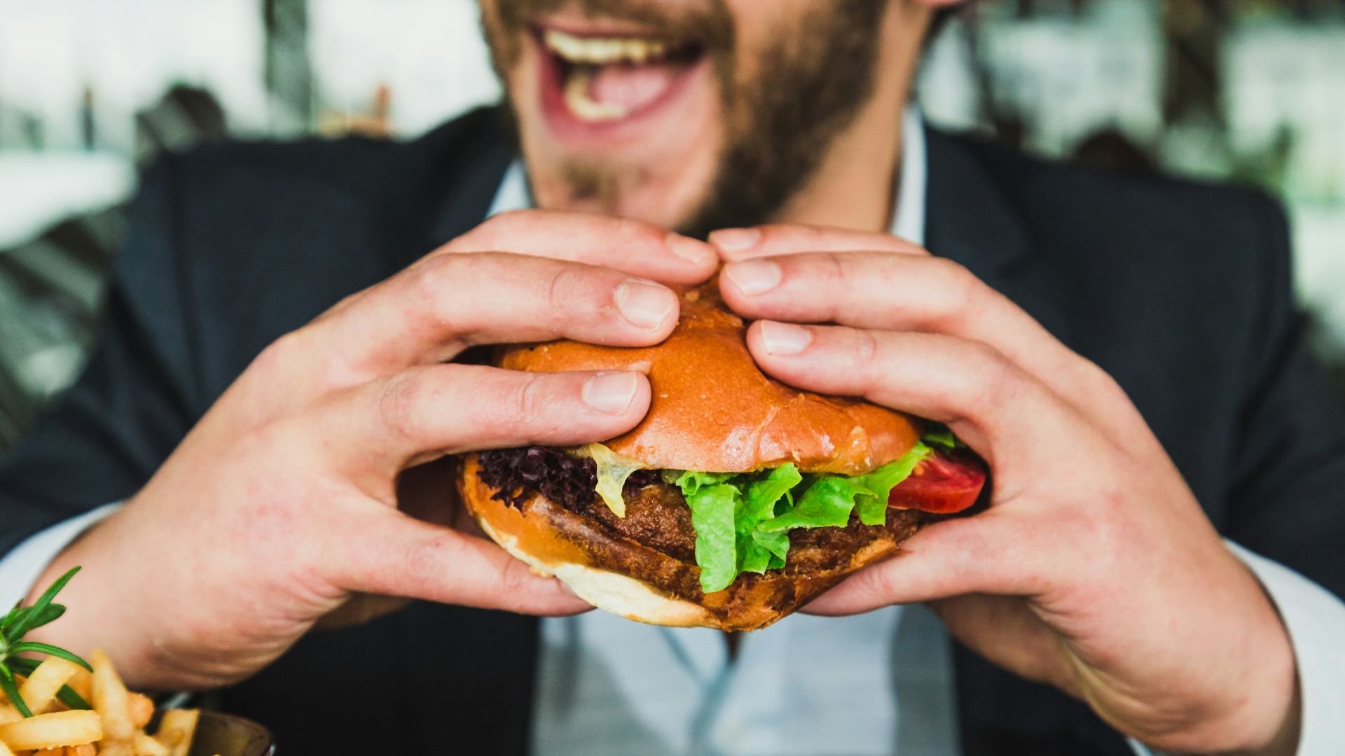 person holding burger bun with vegetables and meat