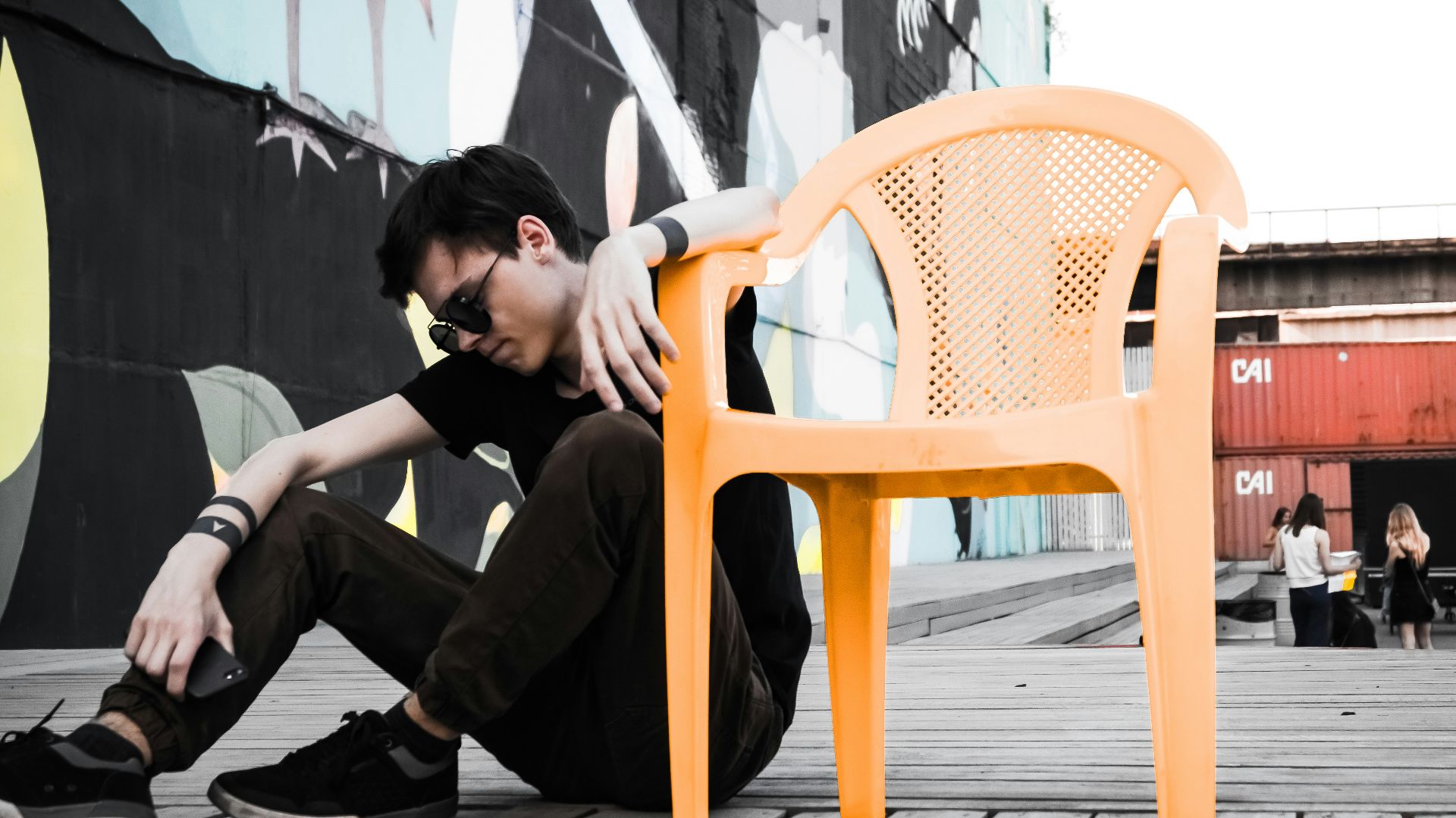 man sitting on floor beside empty orange plastic monobloc armchair at daytime