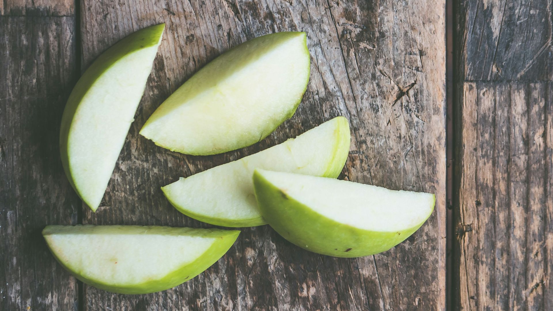 five green apple slices on brown wooden panel