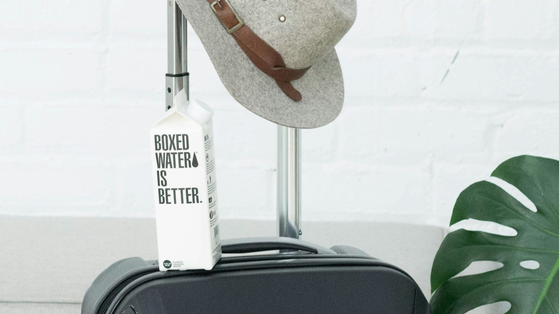 A hat and Boxed Water carton sit on a suitcase