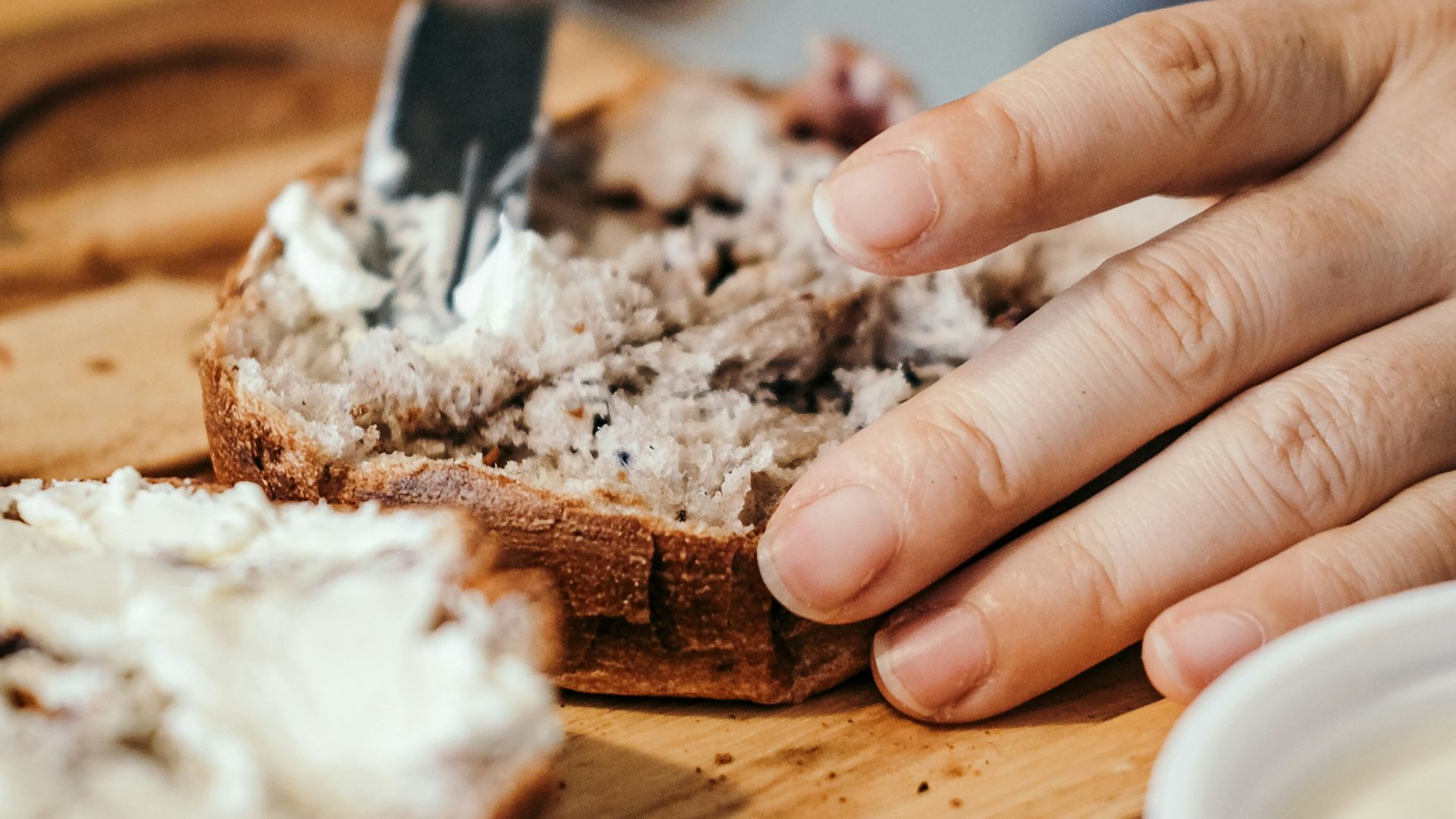person slicing a bread on a brown wooden chopping board