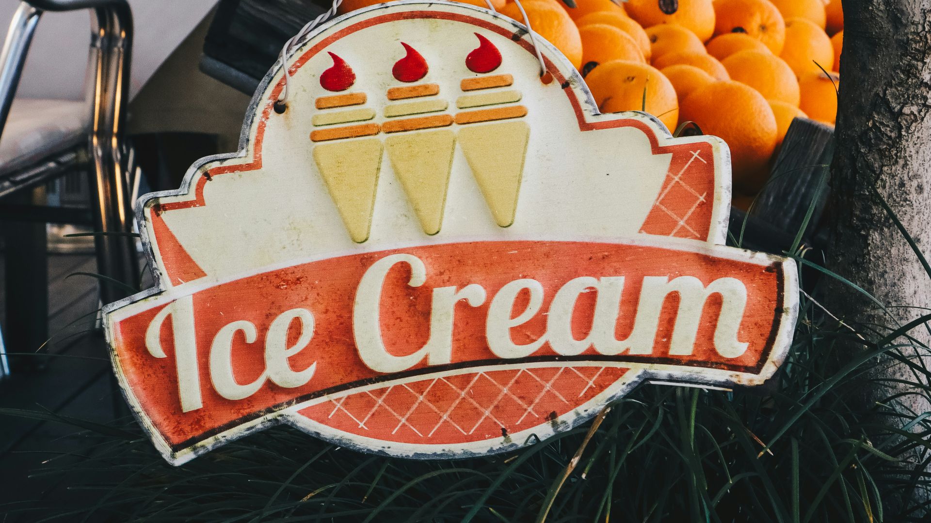 an ice cream sign sitting next to a pile of oranges