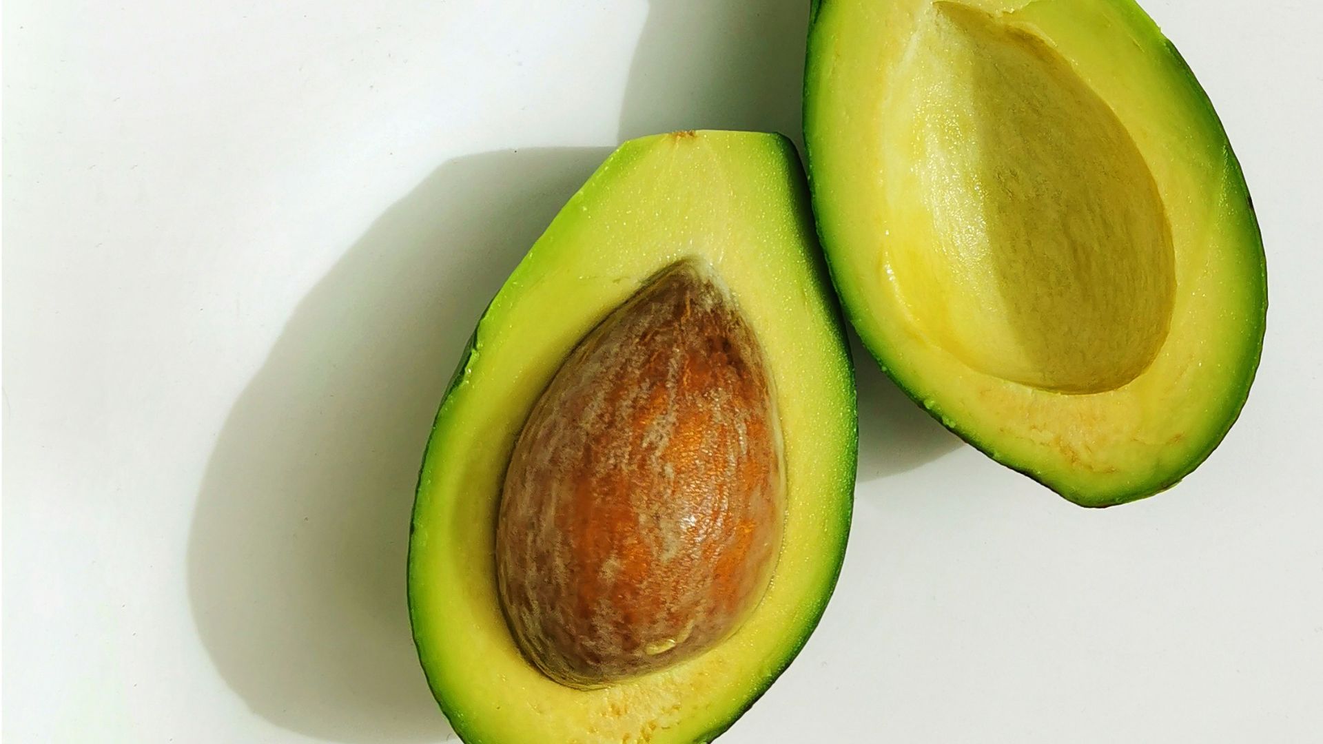 an avocado cut in half on a white surface