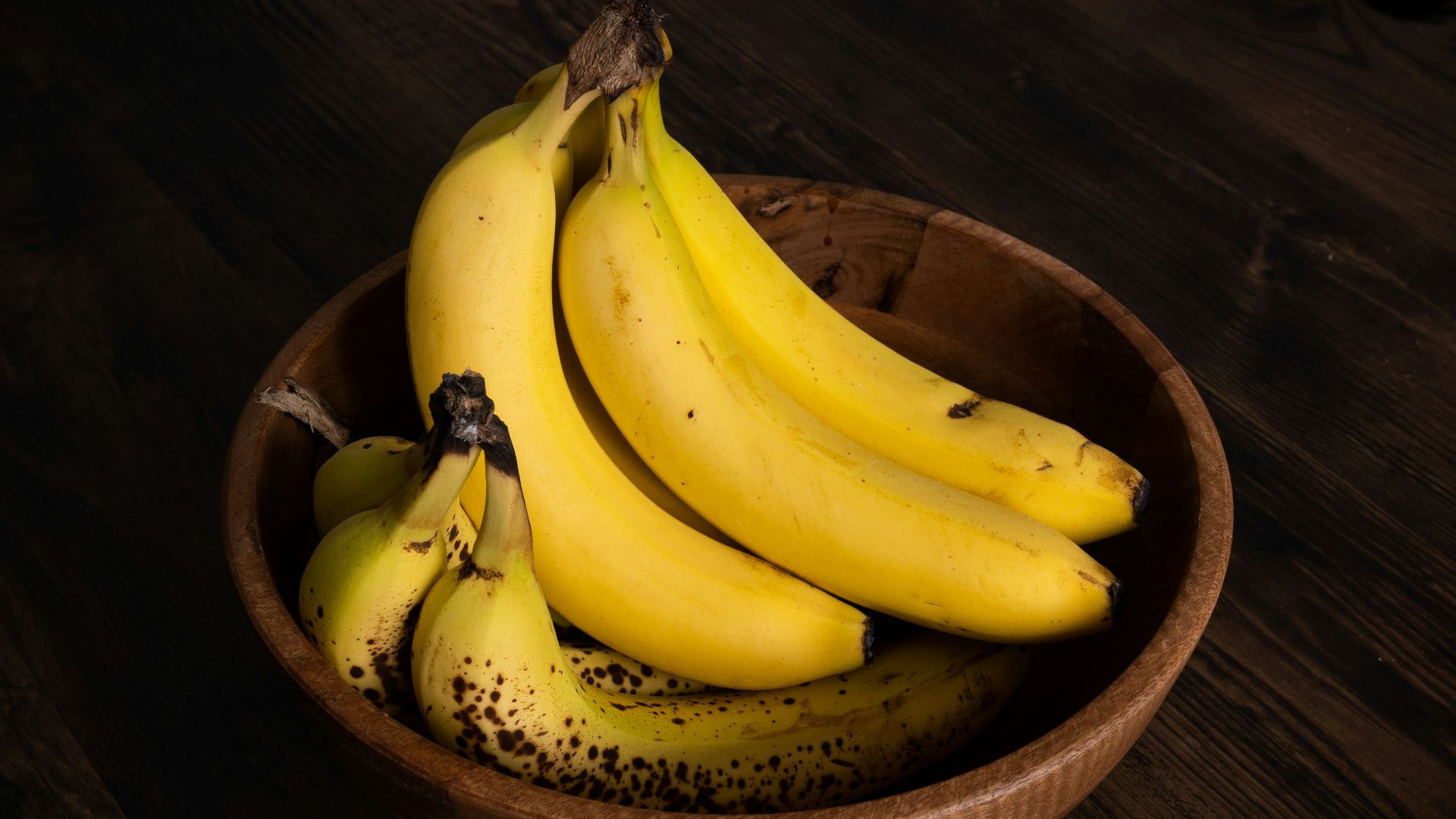 a wooden bowl filled with ripe bananas on top of a wooden table
