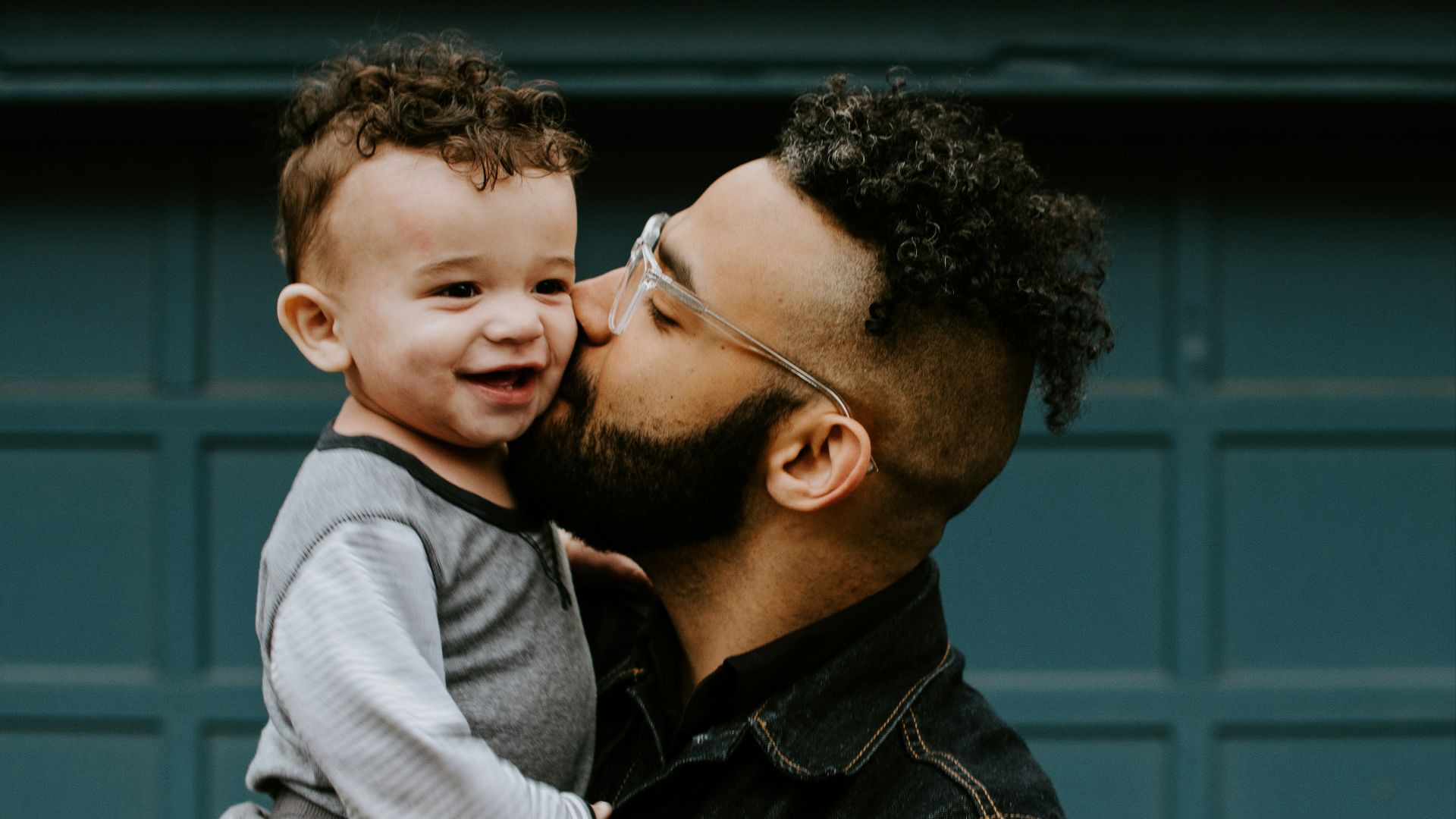 man carrying baby boy and kissing on cheek