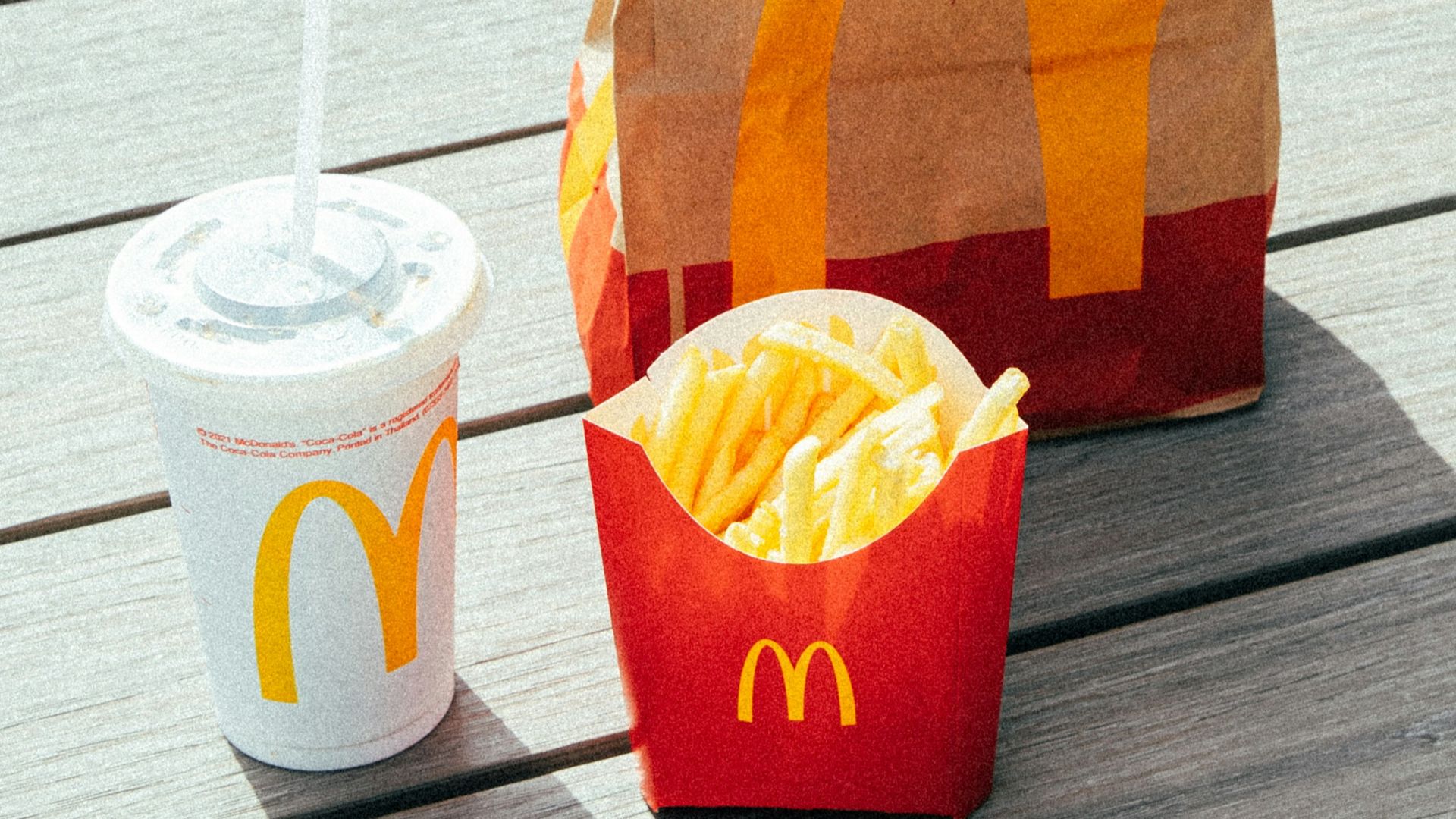 a mcdonald's bag sitting on a wooden deck next to a cup of coffee