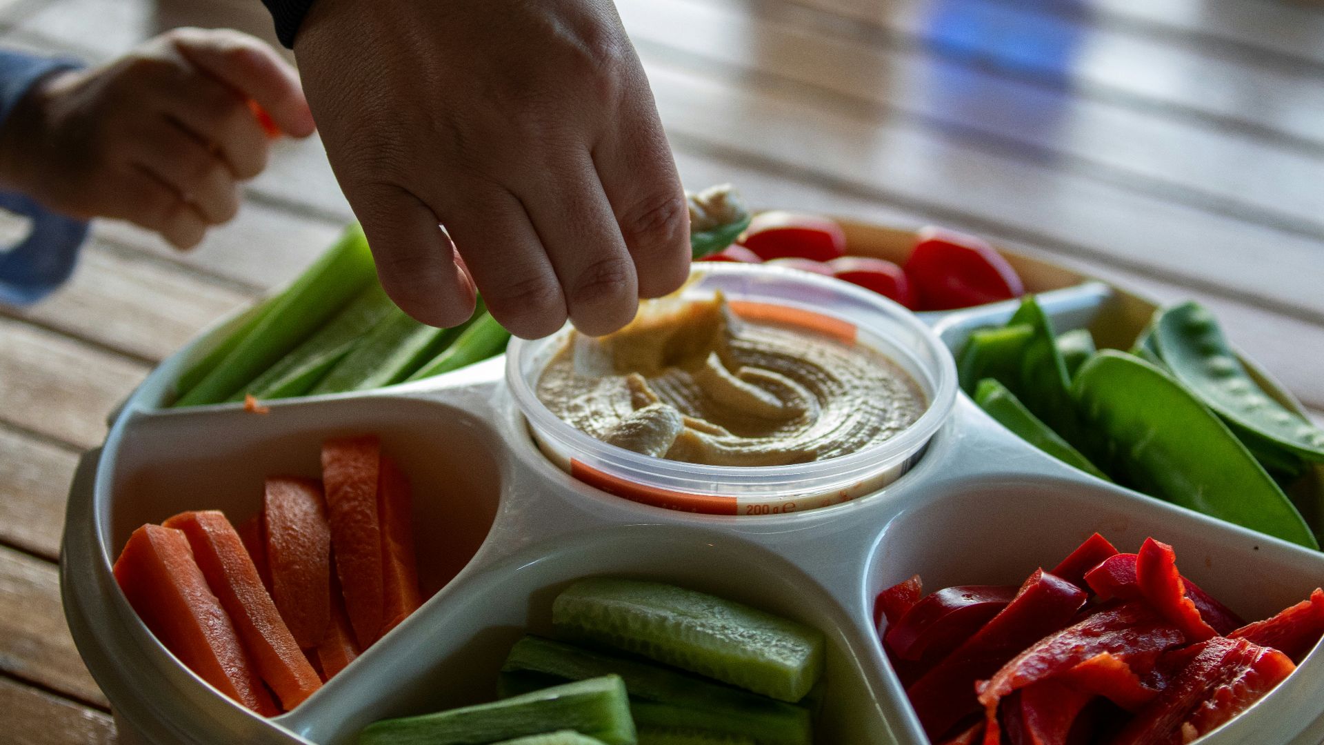 A person dipping dip into a bowl of vegetables