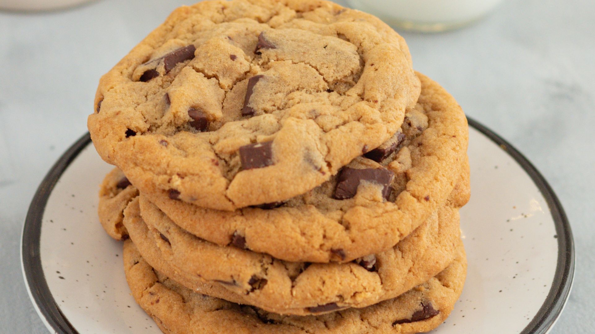 a stack of chocolate chip cookies on a plate next to a glass of milk