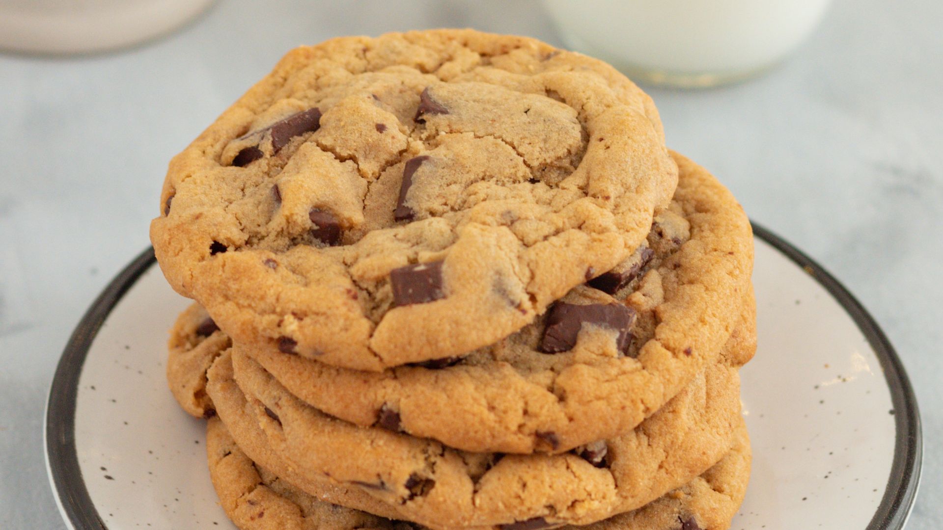 a stack of chocolate chip cookies on a plate next to a glass of milk