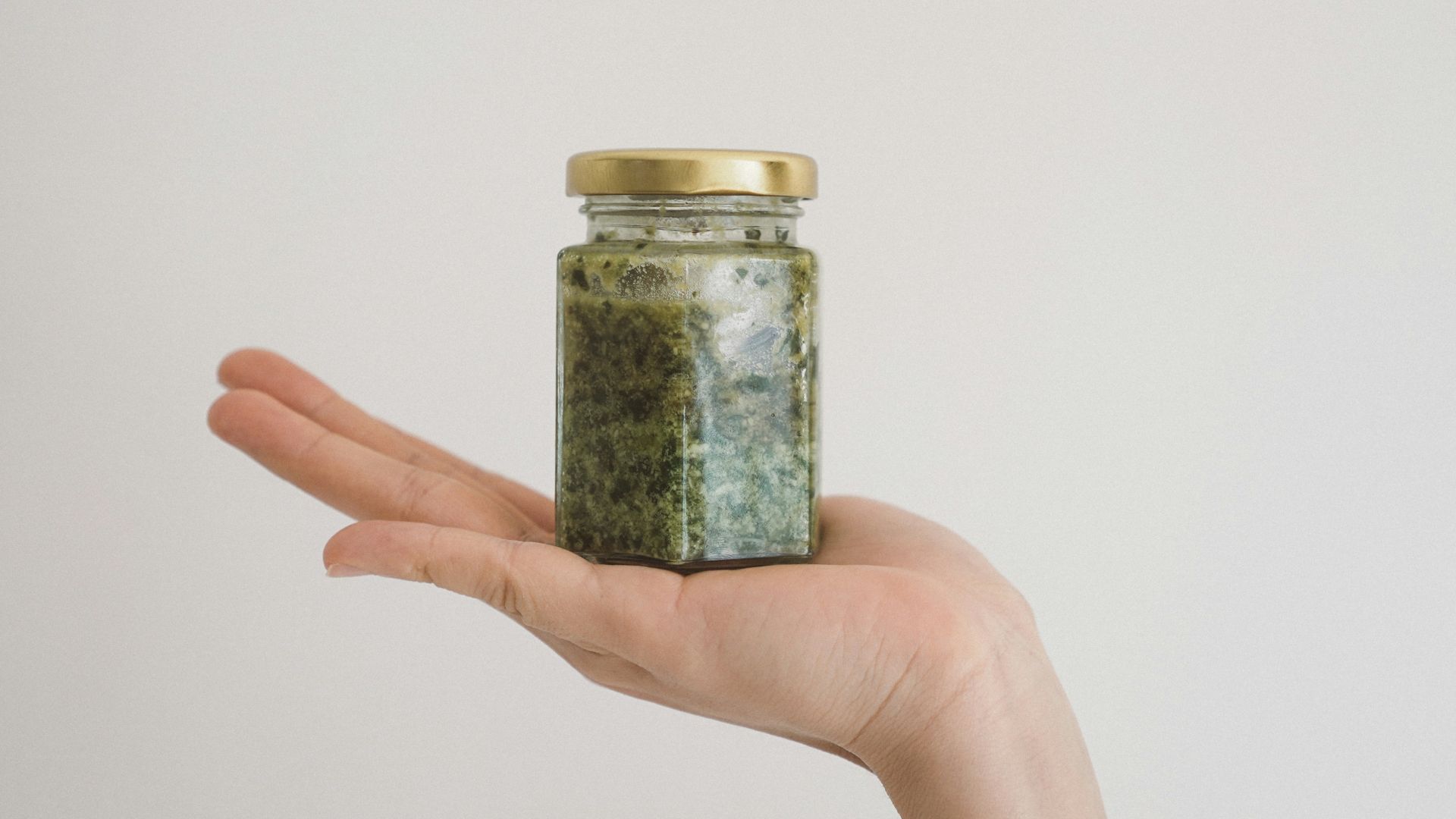 person holding green kush in glass jar
