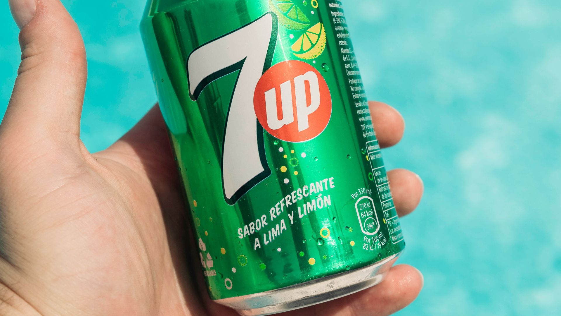 a hand holding a can of 7up by a pool