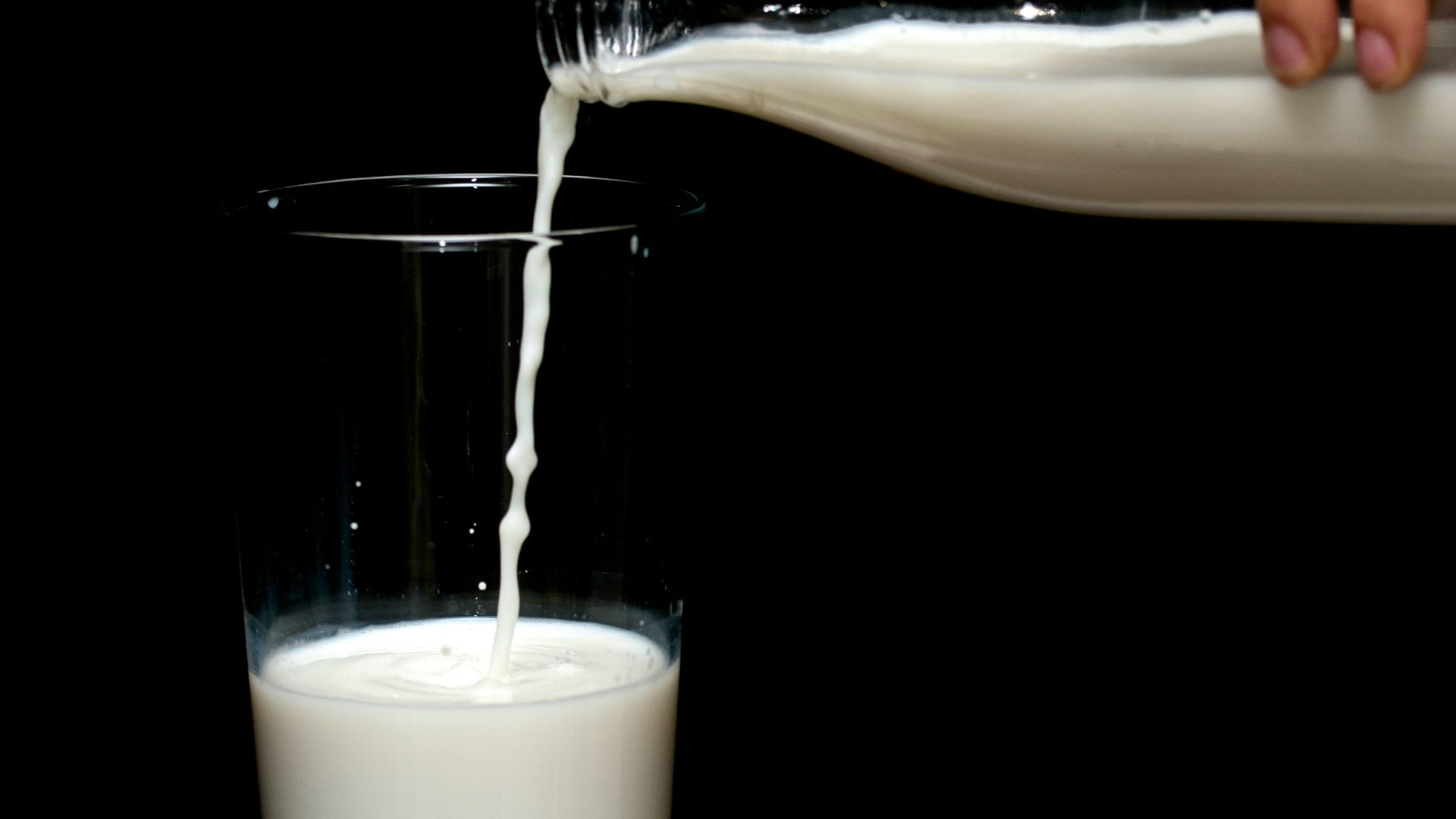 person pouring milk on clear drinking glass