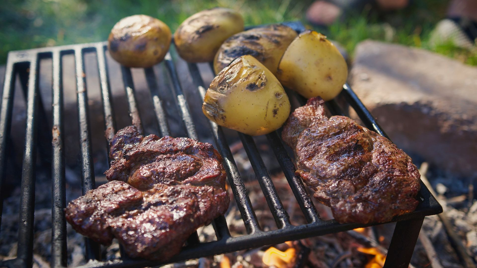 Steaks and potatoes are cooking on a grill