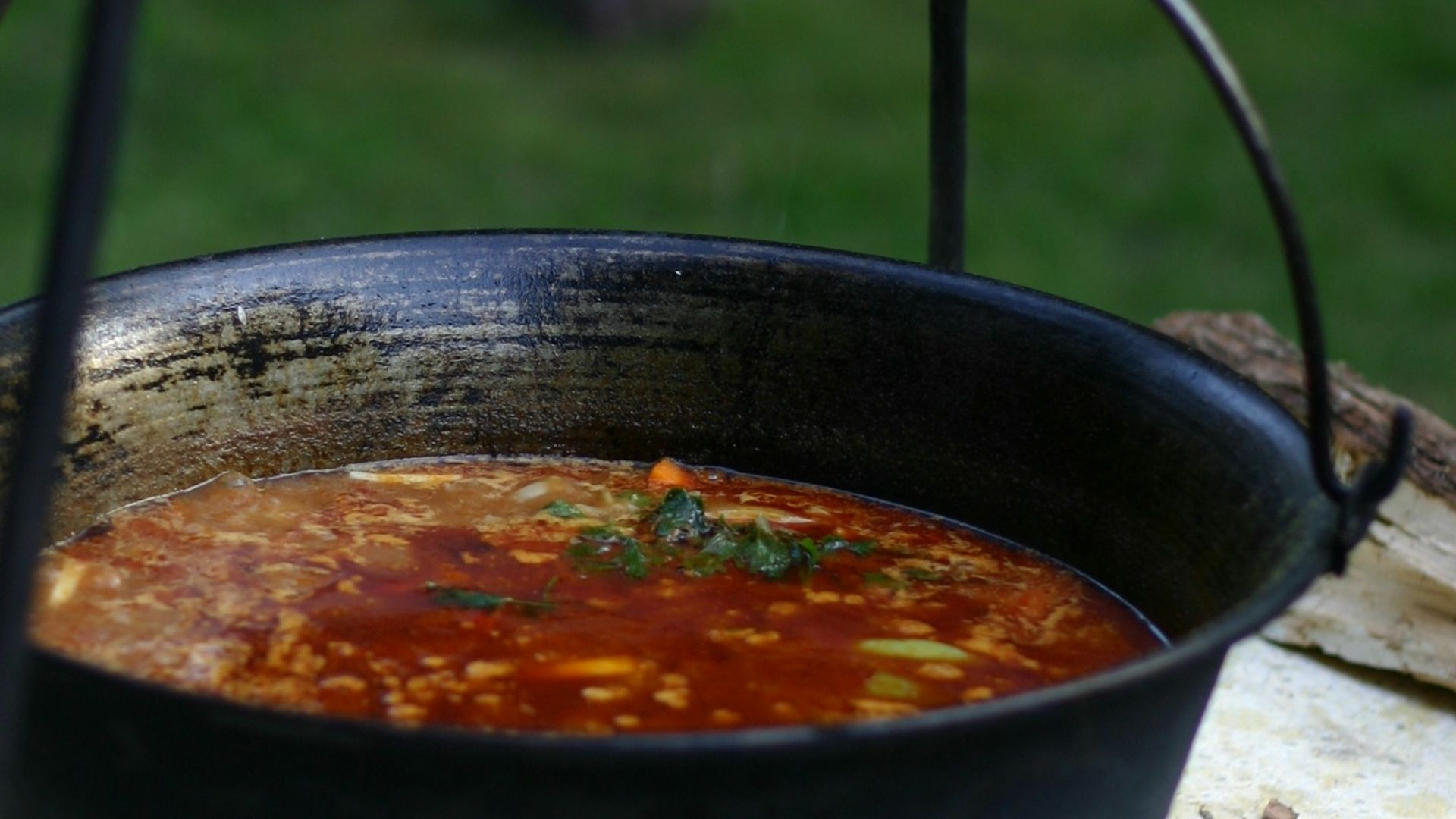 Soup is being cooked in a large hanging pot.
