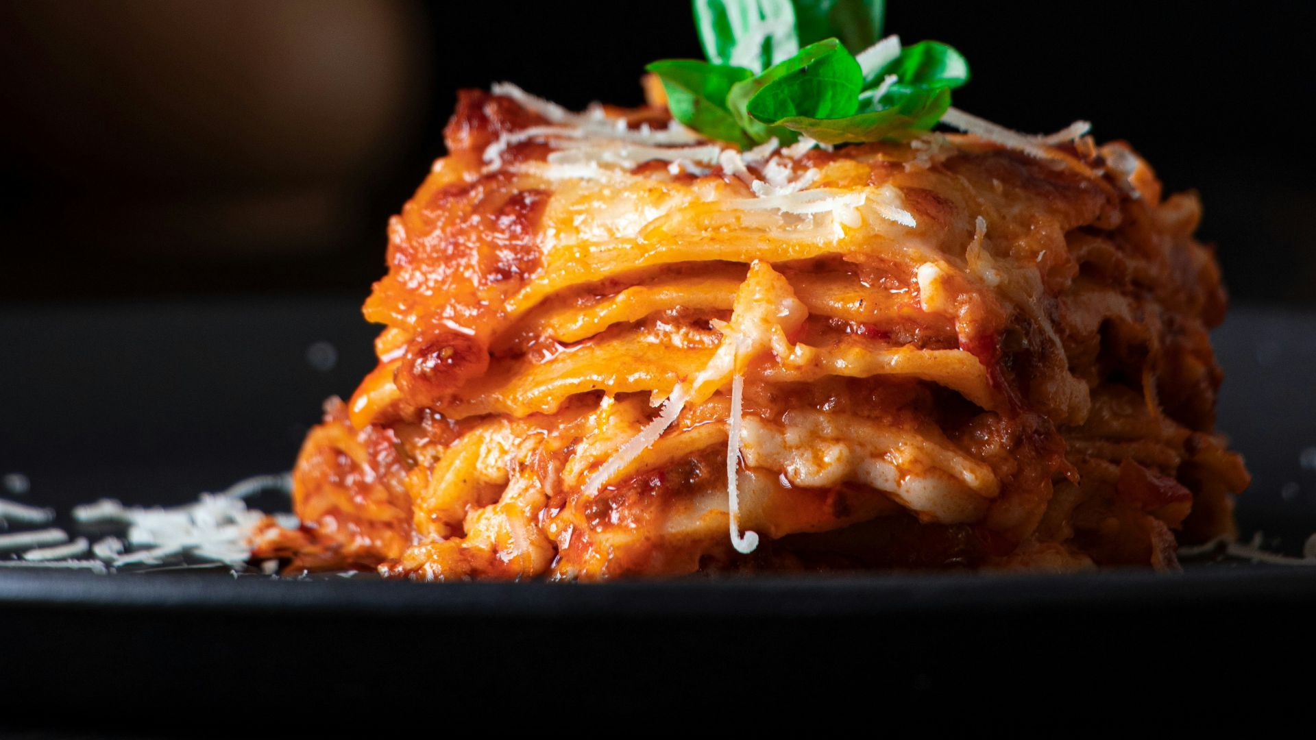 A black plate topped with lasagna covered in sauce and cheese