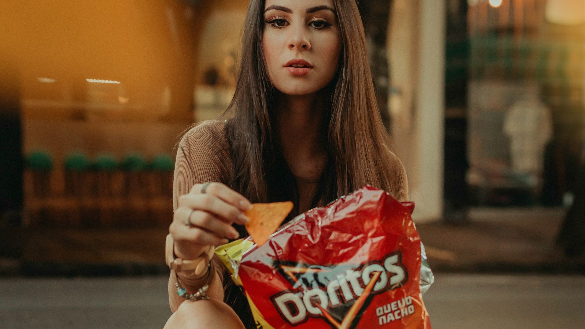 woman in brown shirt sitting on the street holding red and white plastic pack during daytime