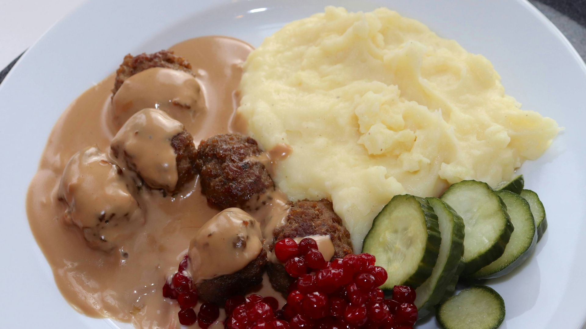 a white plate topped with meatballs, mashed potatoes and cucumbers