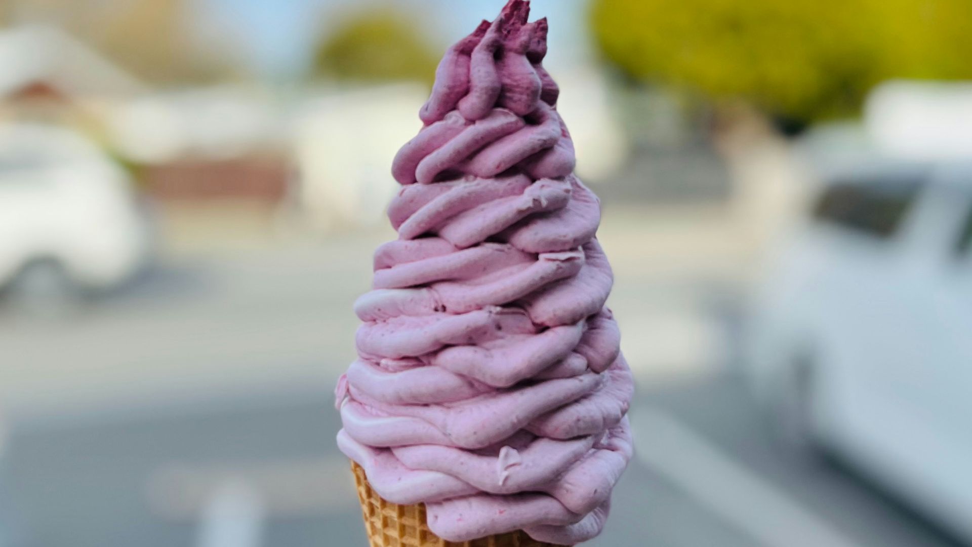 A person holding a pink ice cream cone in a parking lot