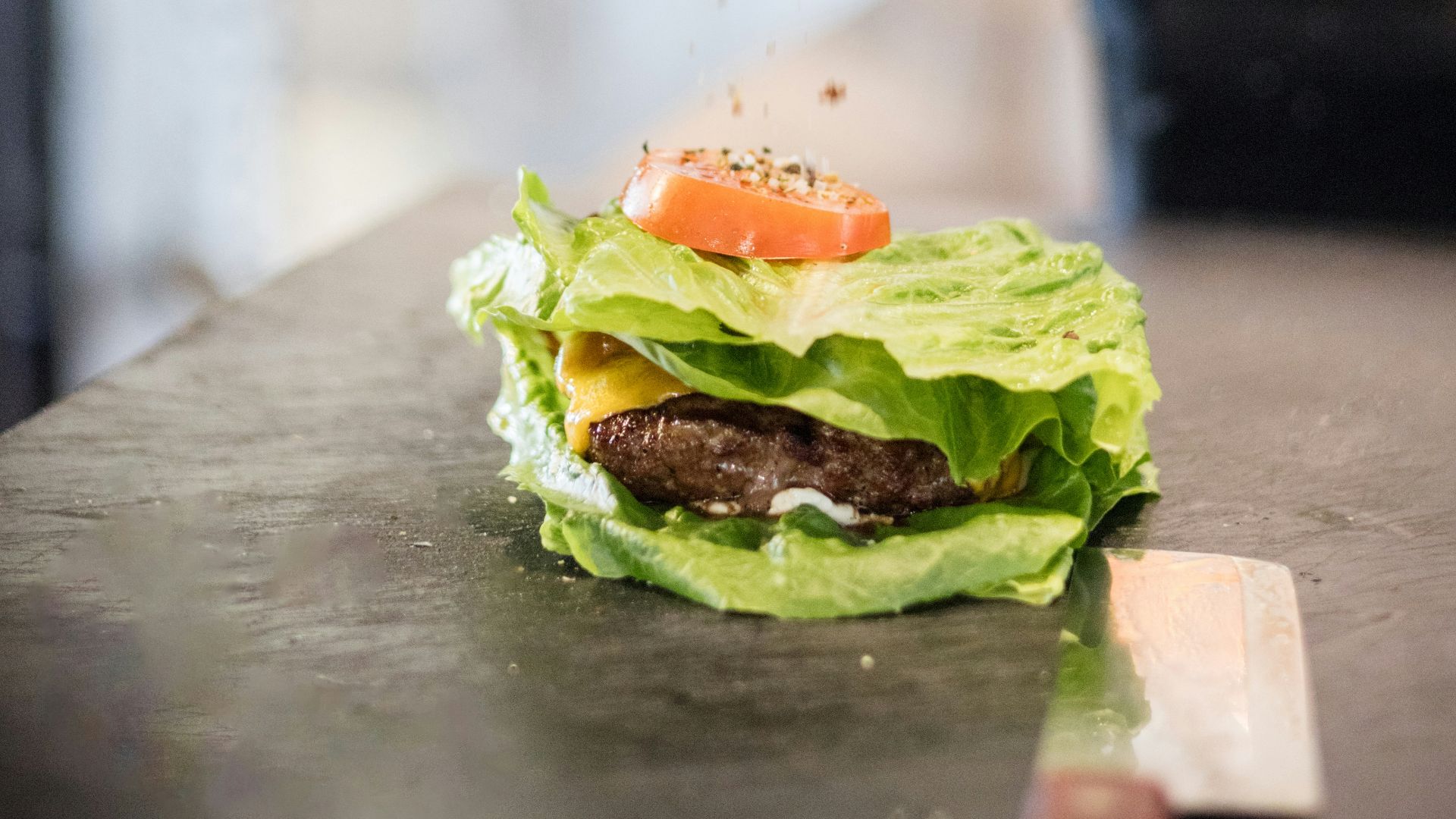 a person sprinkling a piece of food on top of a burger