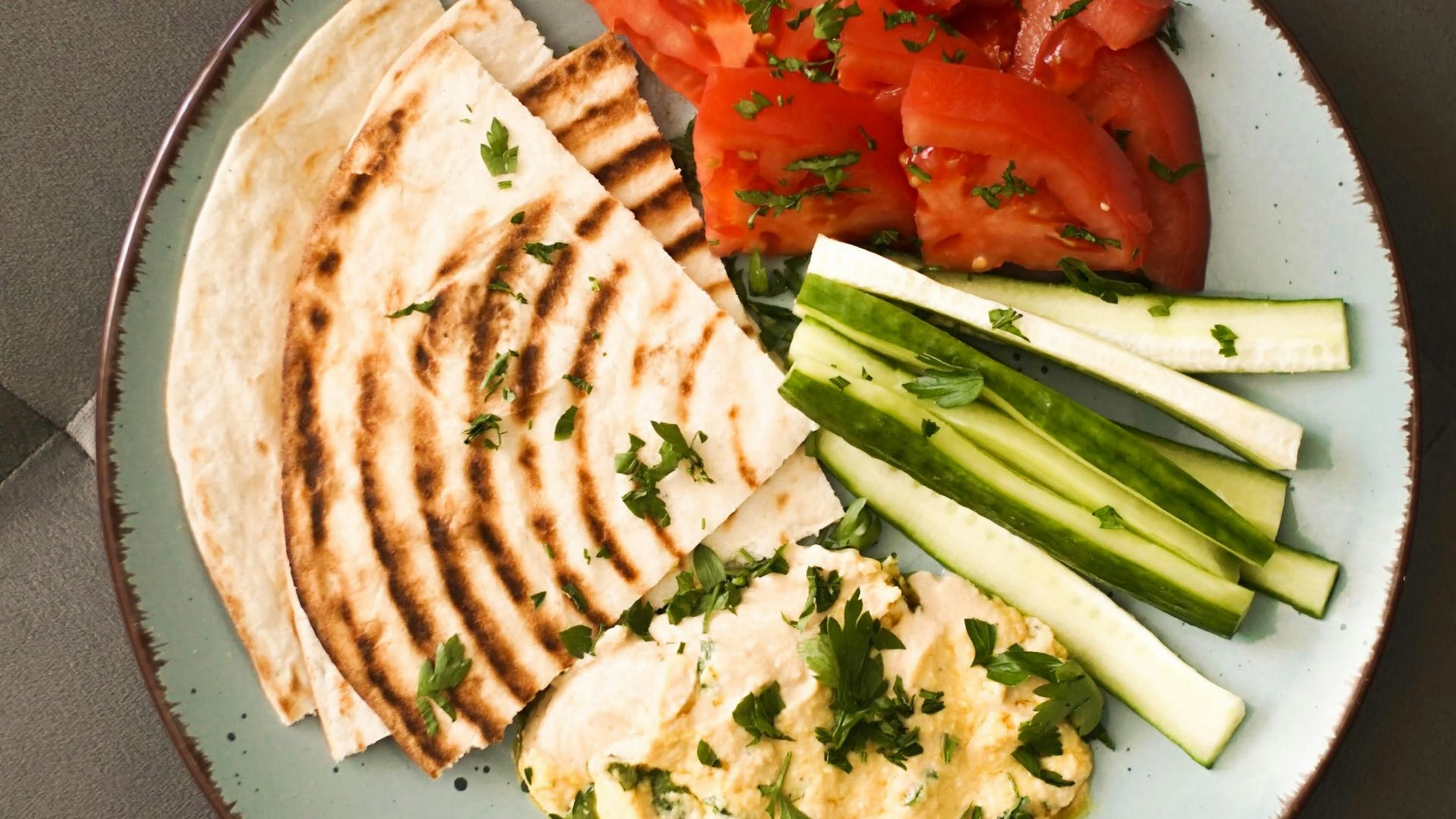 a plate of food that includes pita bread, tomatoes and cucumbers