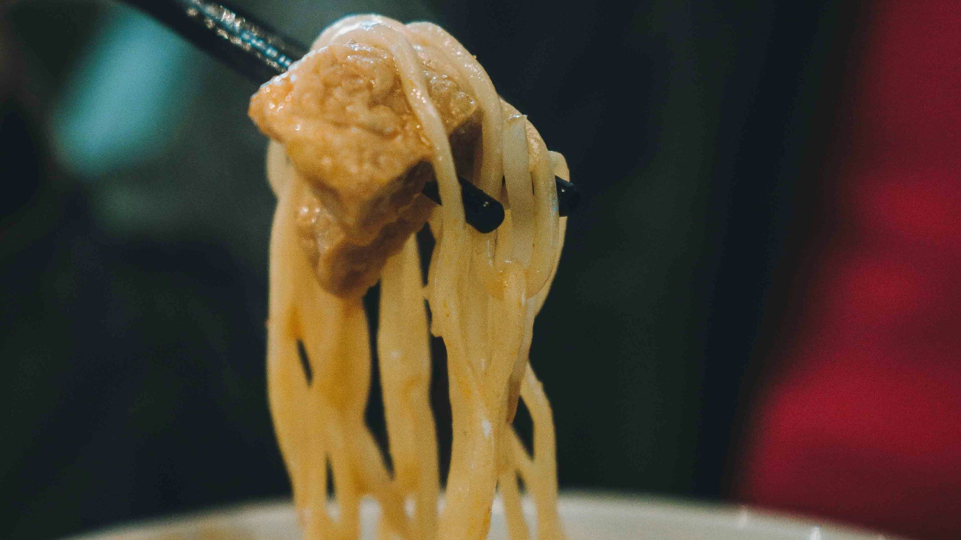 A person holding a spoon full of noodles