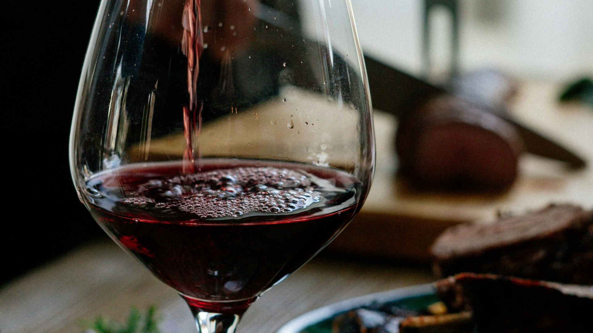 person pouring red wine on wine glass