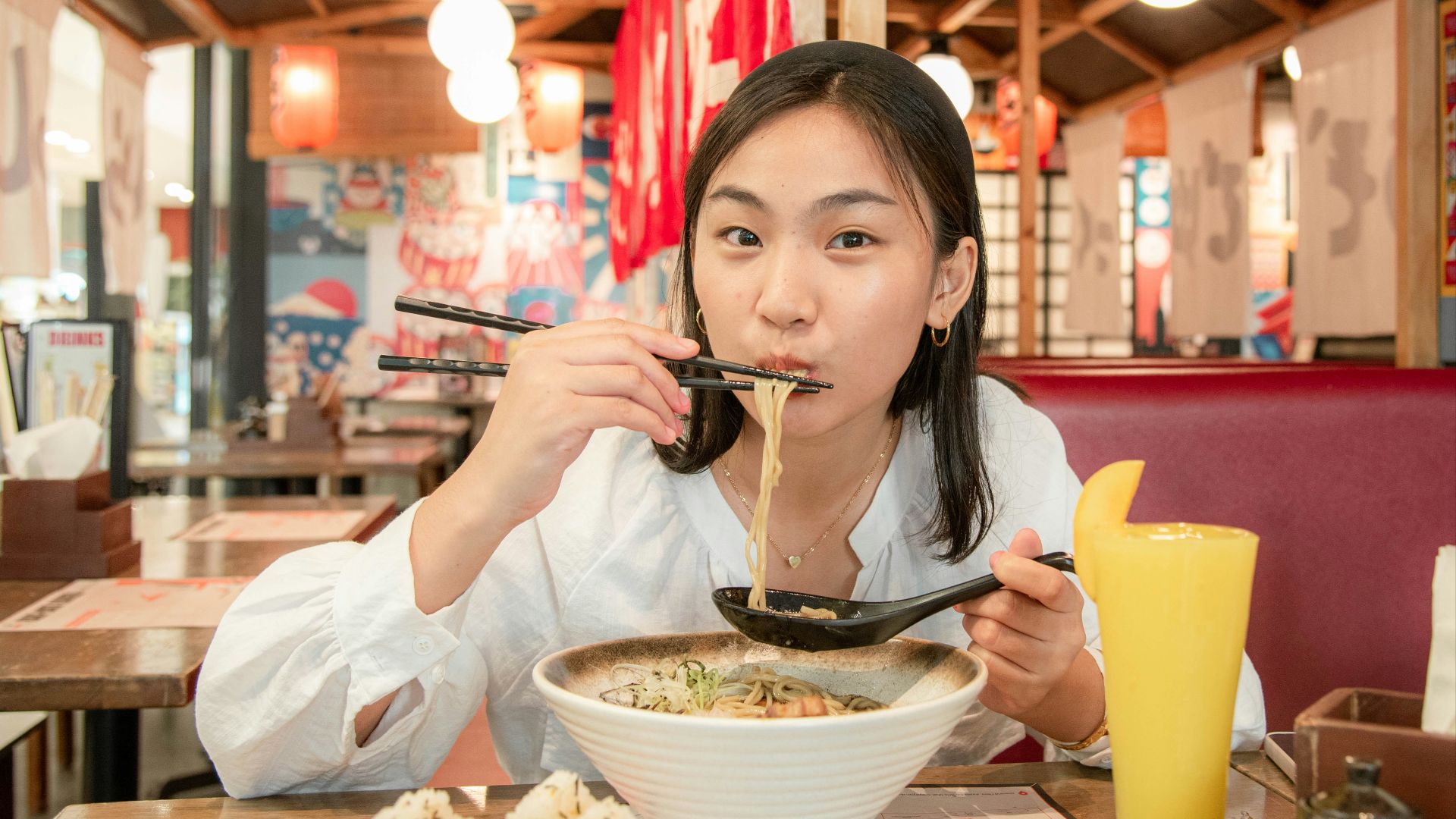 a woman eating noodles with chopsticks at a restaurant