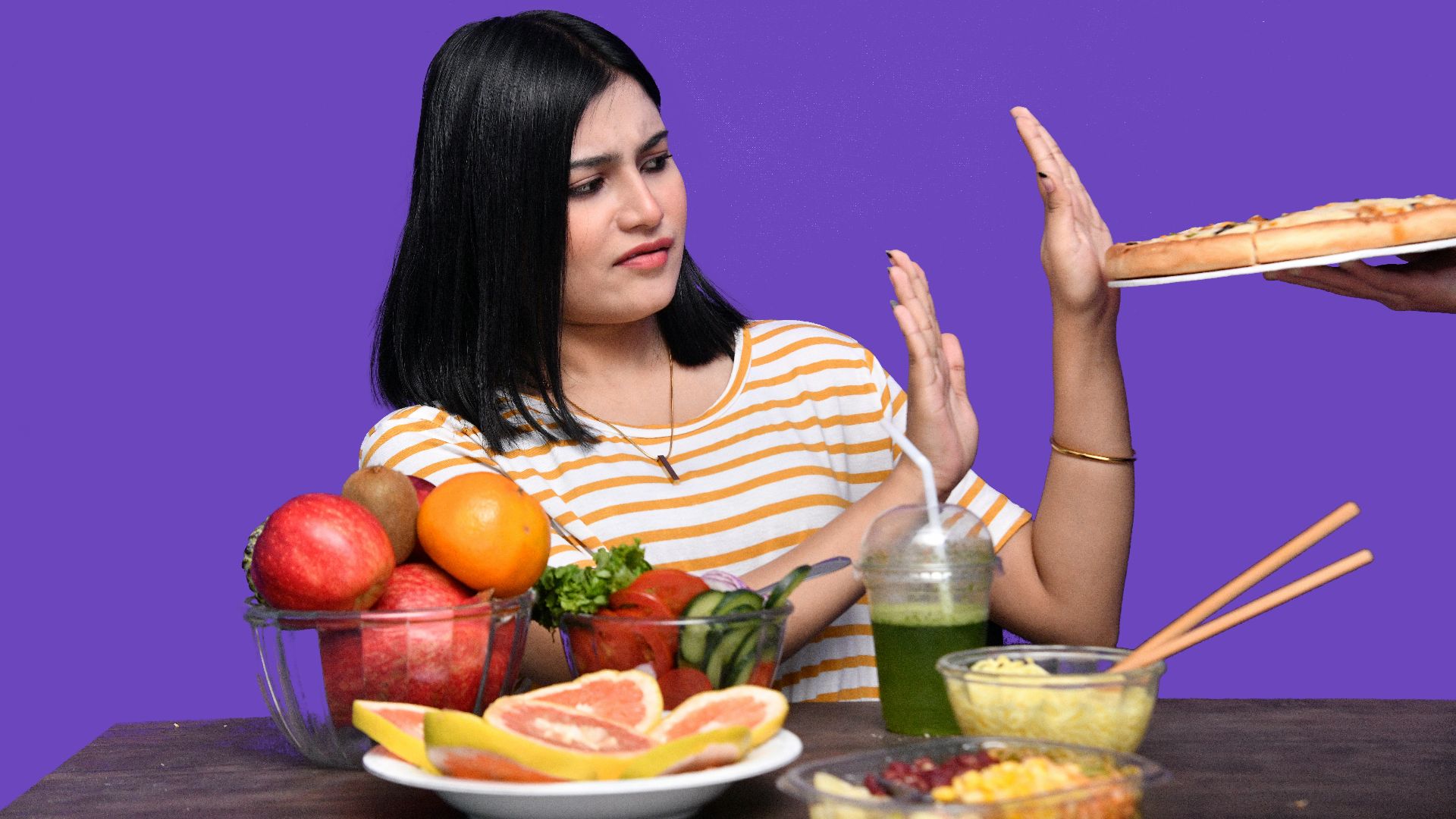 a woman sitting at a table with food and a bowl of fruit